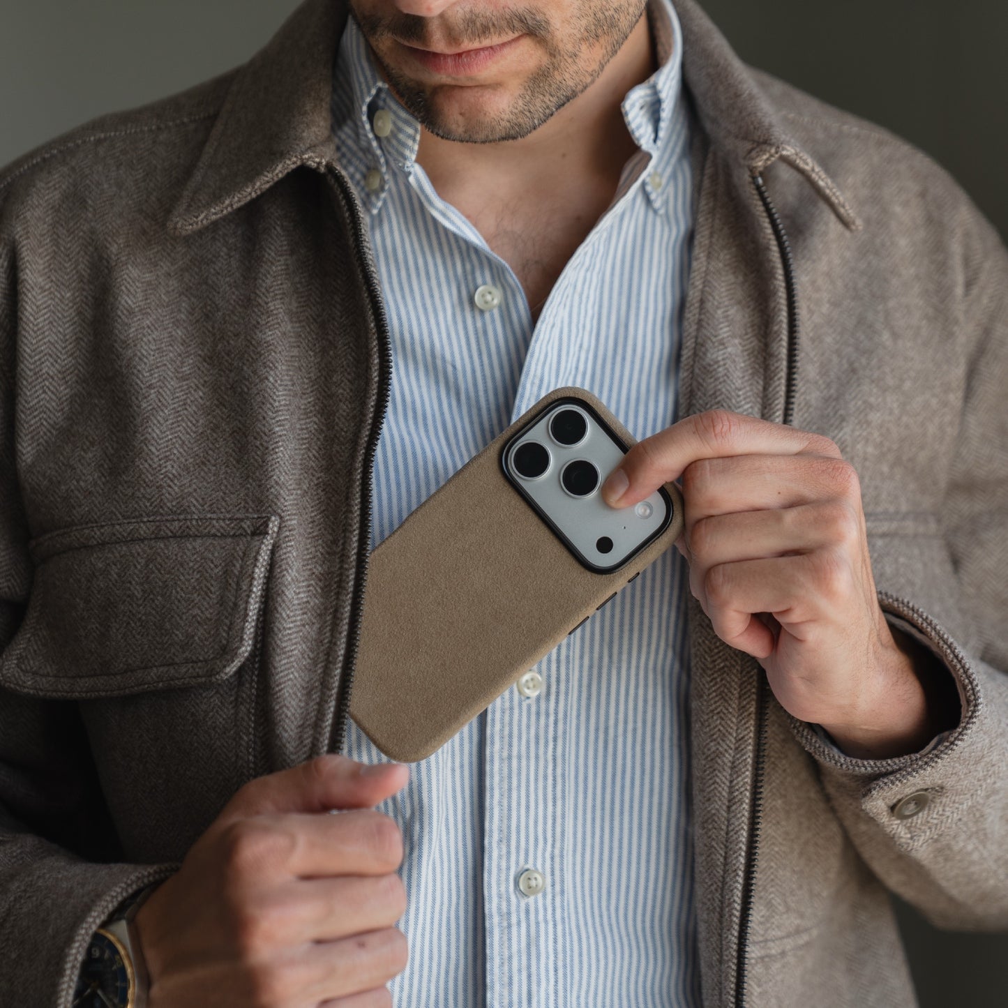 Ein Mann in einer braunen Jacke steckt sein Smartphone mit der arktis iPhone 17 Pro Hülle aus Alcantara, made in Italy, in seine Brusttasche.