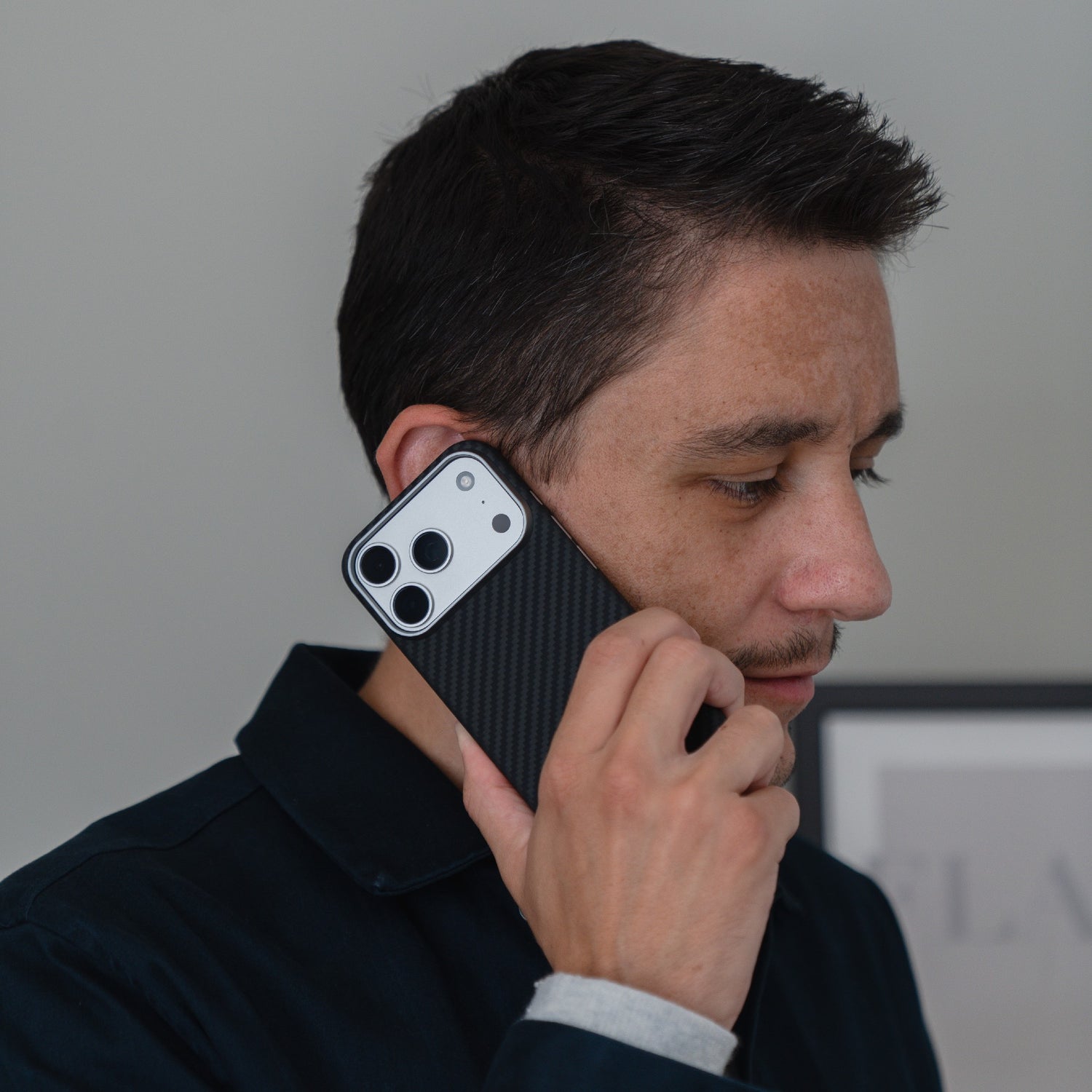 Ein Mann hält sich ein arktis iPhone 17 Pro Carbon Case ans Ohr, als ob er telefonieren würde. Das schlanke arktis Design wird vor einem neutralen Hintergrund präsentiert.