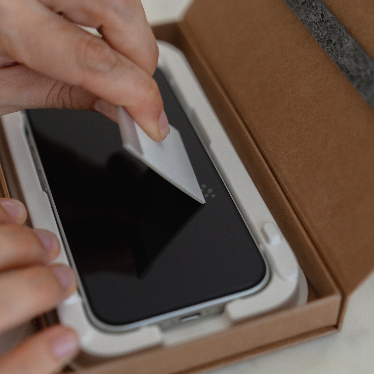 Eine Hand zieht die Schutzfolie von einem arktis 2er Set iPhone 17 Pro Max REVOLUTION Glas-Displayschutz in einer EZ.INSTALL Box ab.