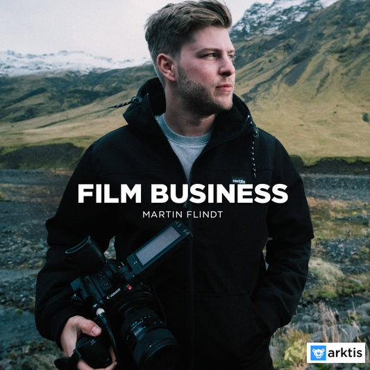 Ein Mann in einer schwarzen Jacke hält eine professionelle Videokamera draußen in den Bergen. Überlagerter Text lautet „Film Business“. Das arktis.de-Logo befindet sich unten rechts – perfekt für Filmemacher und ihren nächsten Online-Kurs.