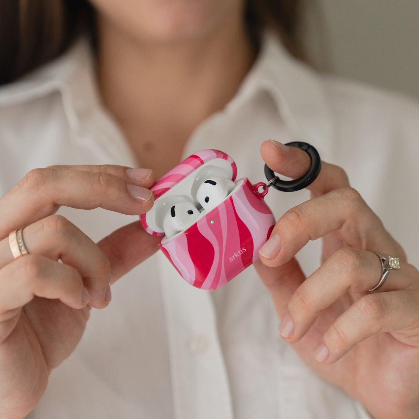 Hände, die kabellose Ohrhörer in einer rosa-rot gemusterten Arktis AirPods 5-Hülle – Aura Pink – halten.