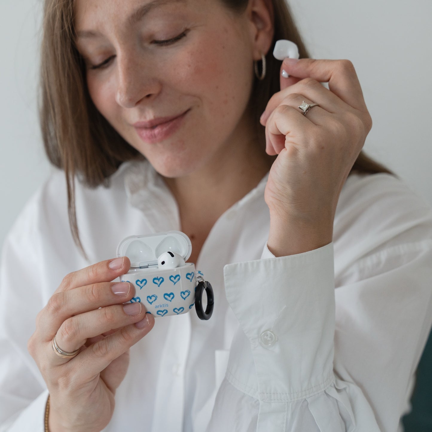 Eine lächelnde Frau hält eine Arktis AirPods 5-Hülle – Blue Hearts – in der Hand und ist bereit, einen AirPod zu benutzen.