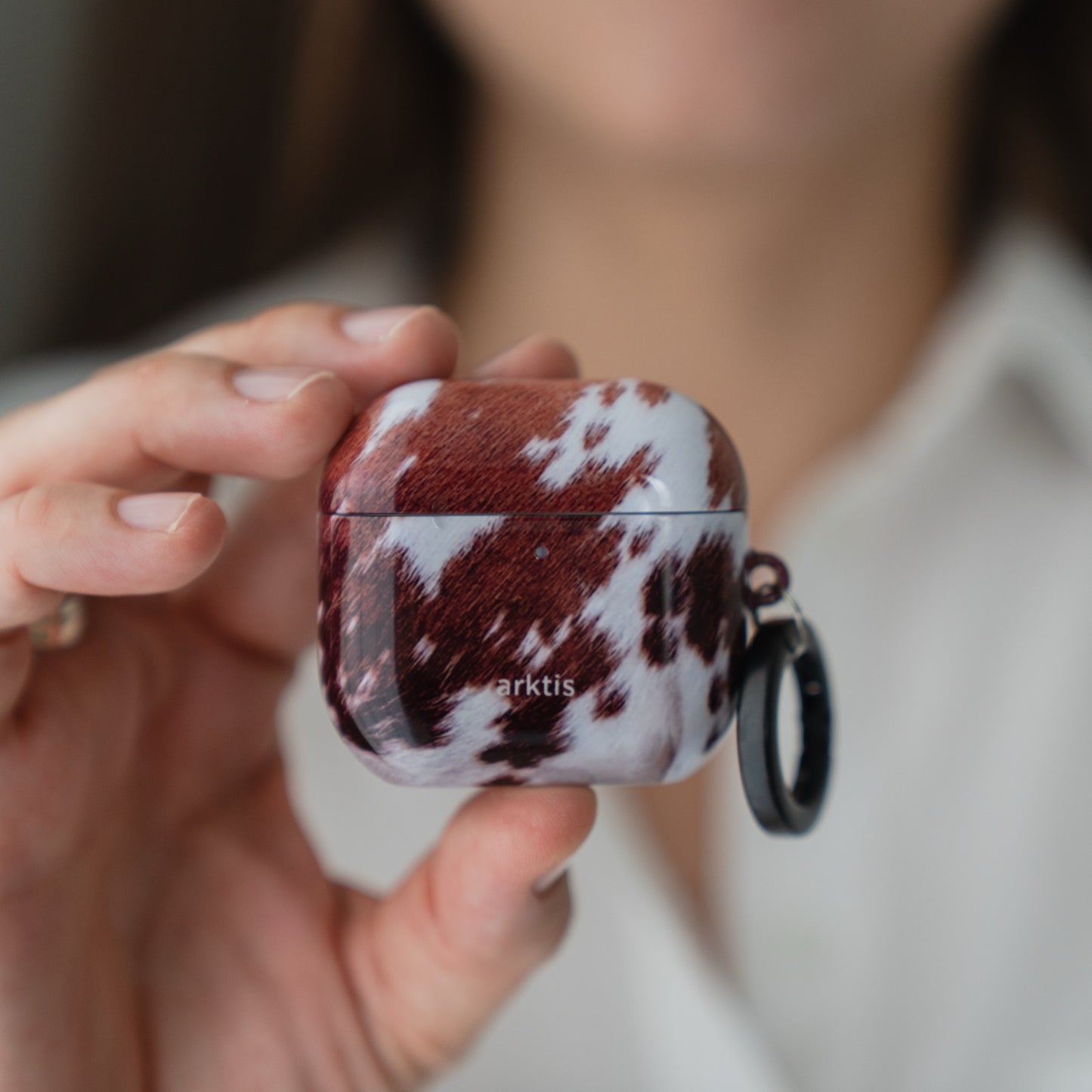 Eine Person, die eine Arktis AirPods 5-Hülle – Cow mit einem braun-weißen Kuhmuster – in der Hand hält.