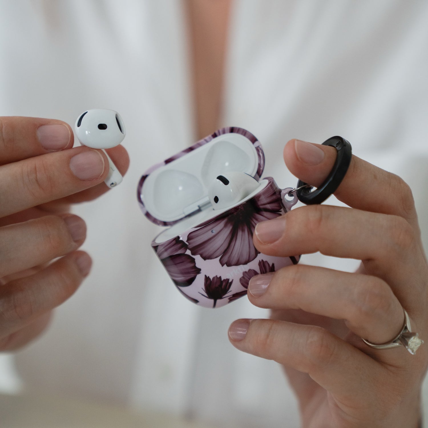 Hände, die eine geöffnete, mit Blumenmustern verzierte Arktis AirPods 5-Hülle – Bloom Case – halten, wobei ein Ohrhörer herausgenommen ist.