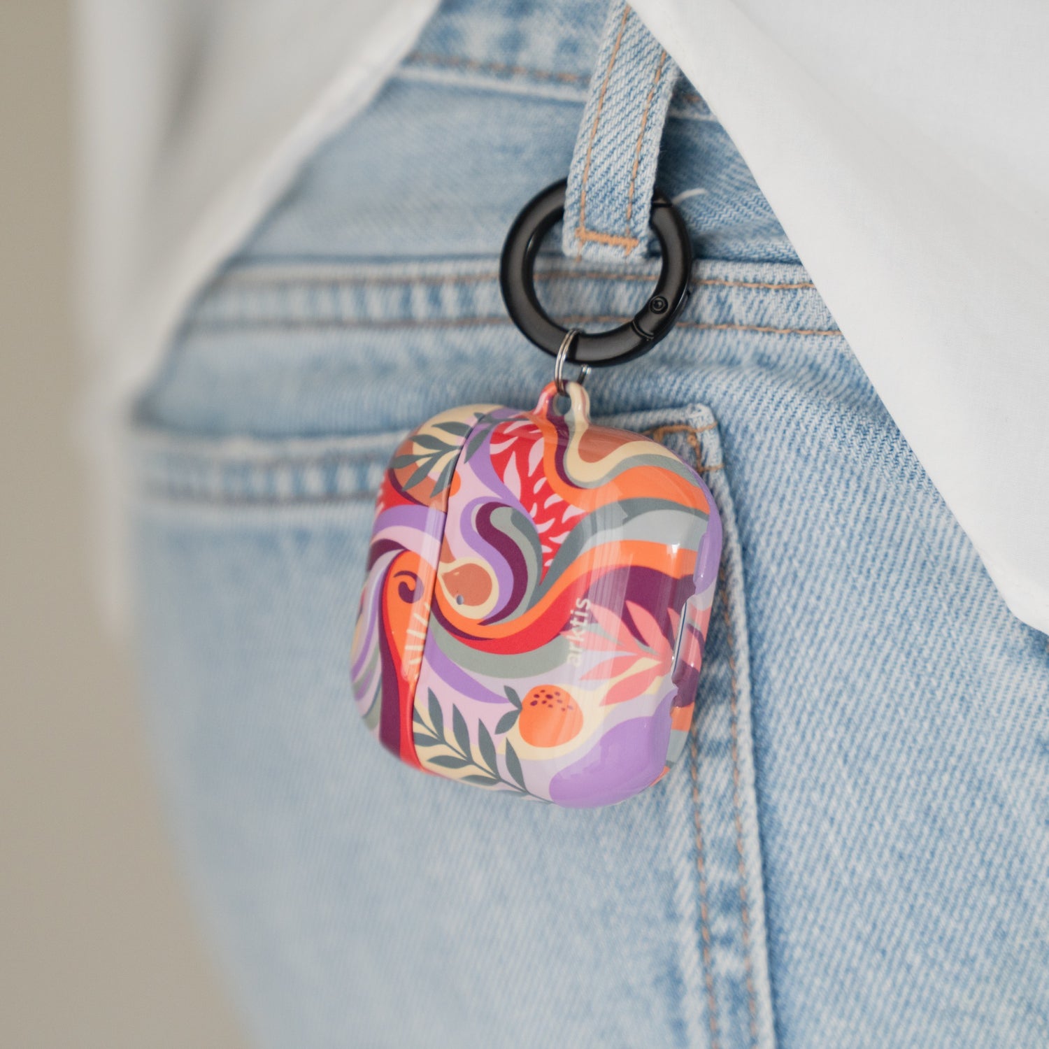 Arktis AirPods 5 Hülle – Summer mit einem farbenfrohen, abstrakten Muster, die mit einem schwarzen Karabinerhaken an einer Jeans-Gürtelschlaufe befestigt ist.