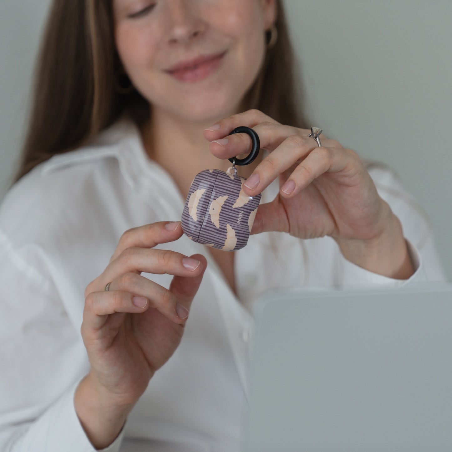 Eine Frau, die eine Arktis AirPods 5-Hülle in der Hand hält – French Breakfast mit einem Muster aus violetten und beigen Croissants.