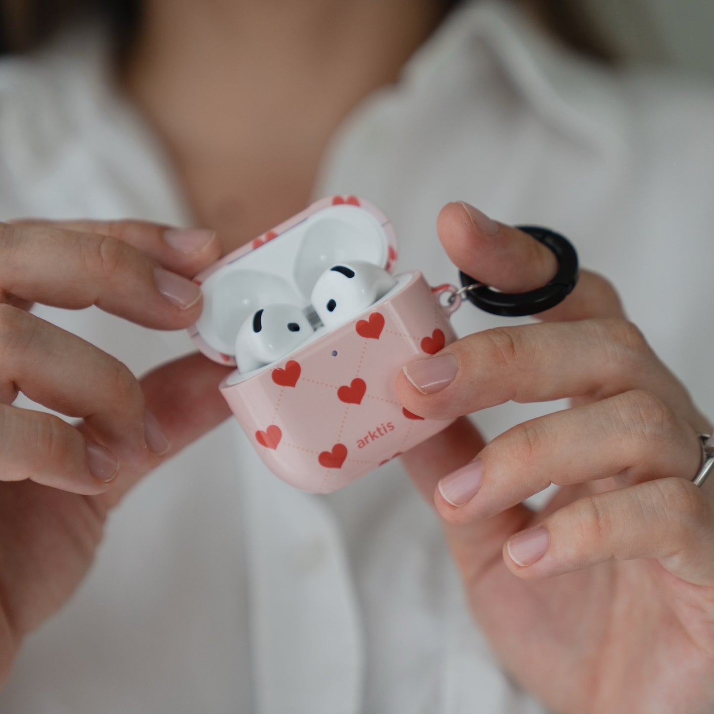 Hände, die eine geöffnete, rosa Arktis AirPods 5-Hülle halten – Love Case mit kleinen roten Herzen als Muster.
