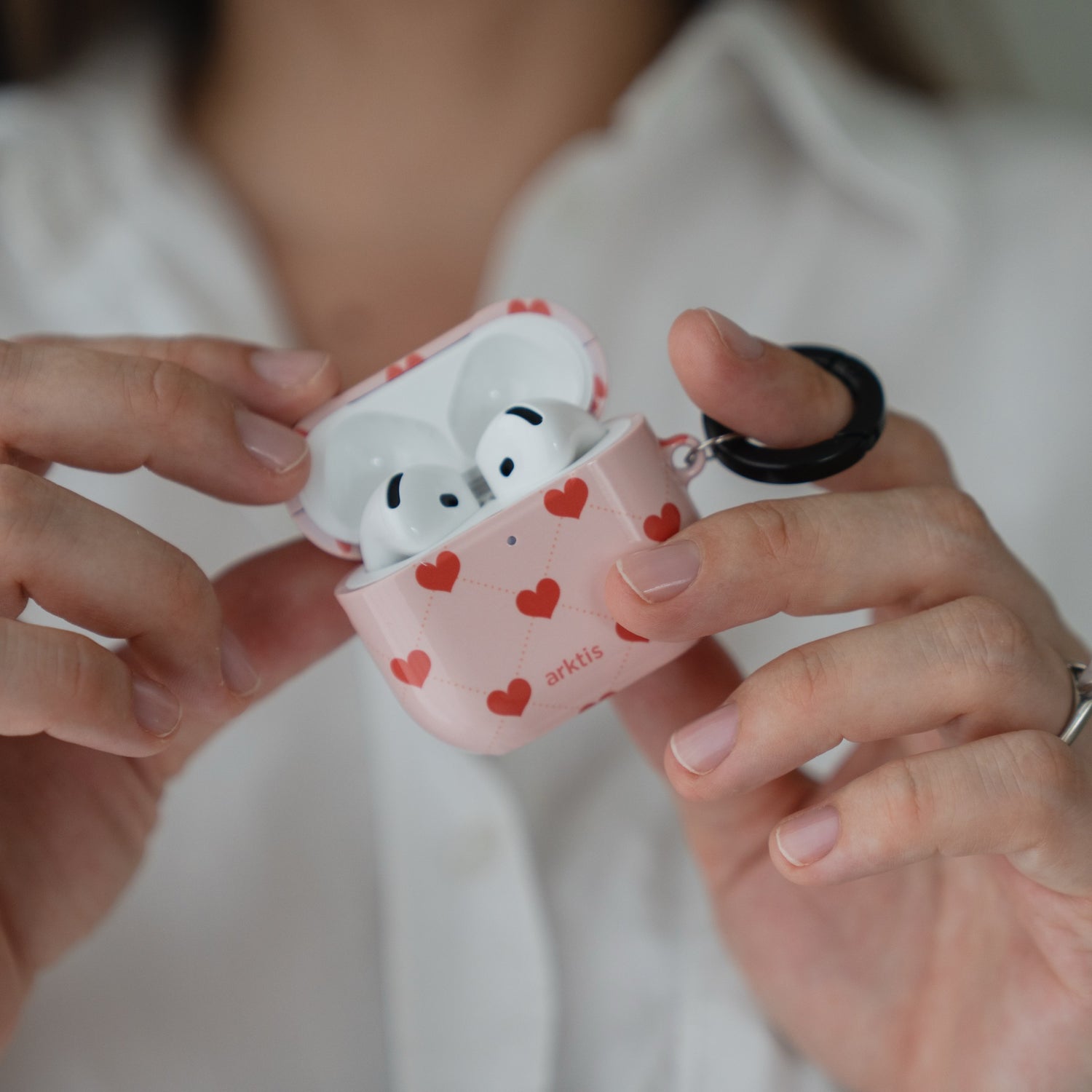 Hände, die eine geöffnete, rosa Arktis AirPods 5-Hülle halten – Love Case mit kleinen roten Herzen als Muster.
