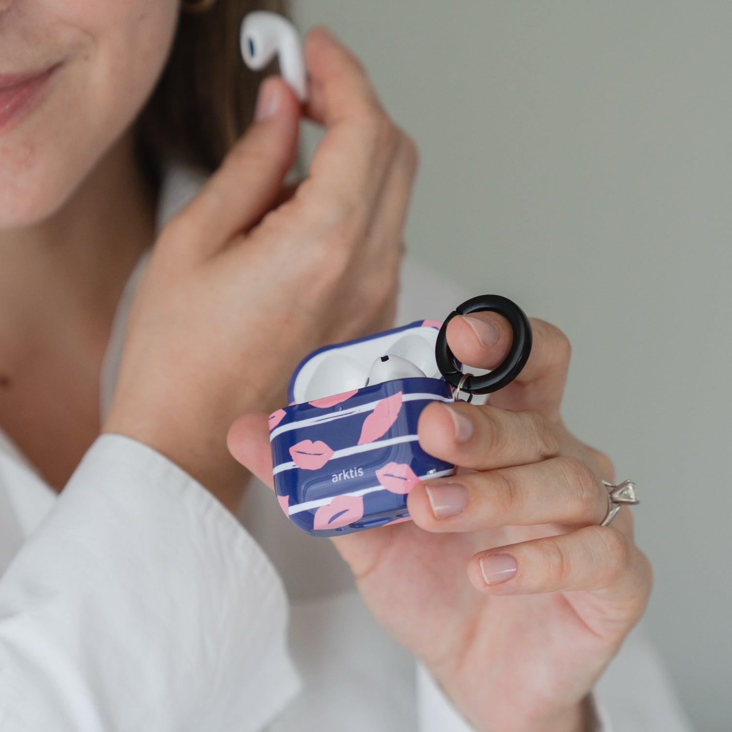 Eine Person hält eine Arktis AirPods 5 Hülle – Kisses Case in der Hand und ist gerade dabei, sich einen AirPod ins Ohr zu stecken.