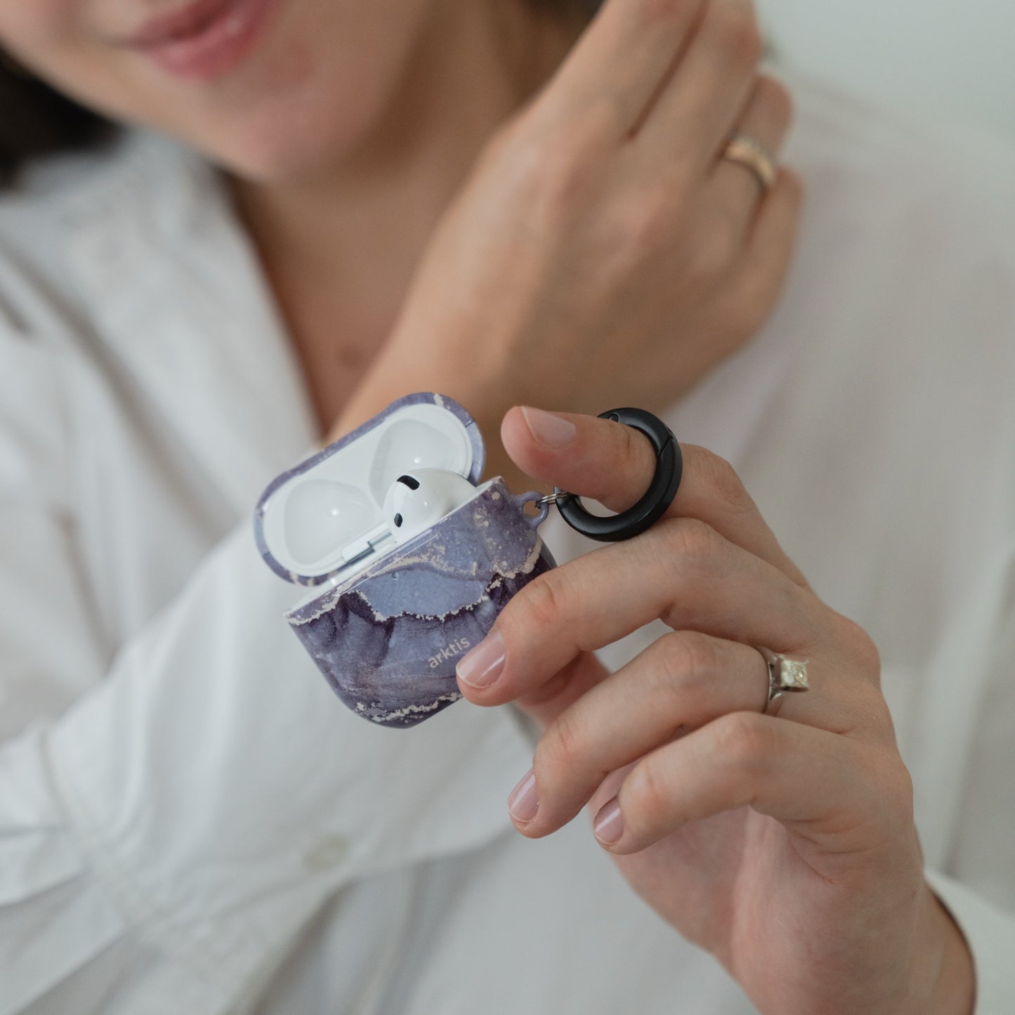 Eine Hand, die eine geöffnete Arktis AirPods 5-Hülle hält – ein Dusty Marble-Case mit violettem Marmormuster und einem schwarzen Befestigungsring.