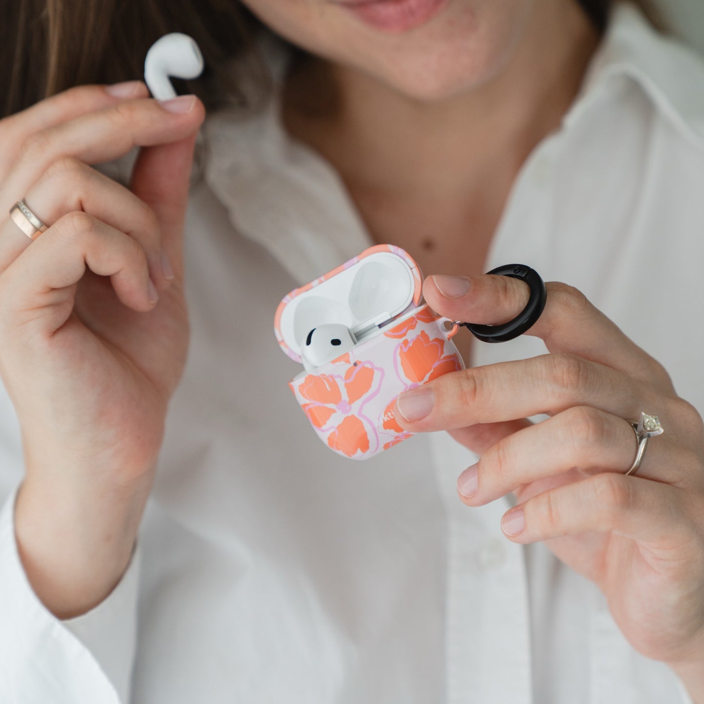 Eine Person, die eine Arktis AirPods 5 Hülle – Orange Mallow mit einem schwarzen Befestigungsring in der Hand hält.