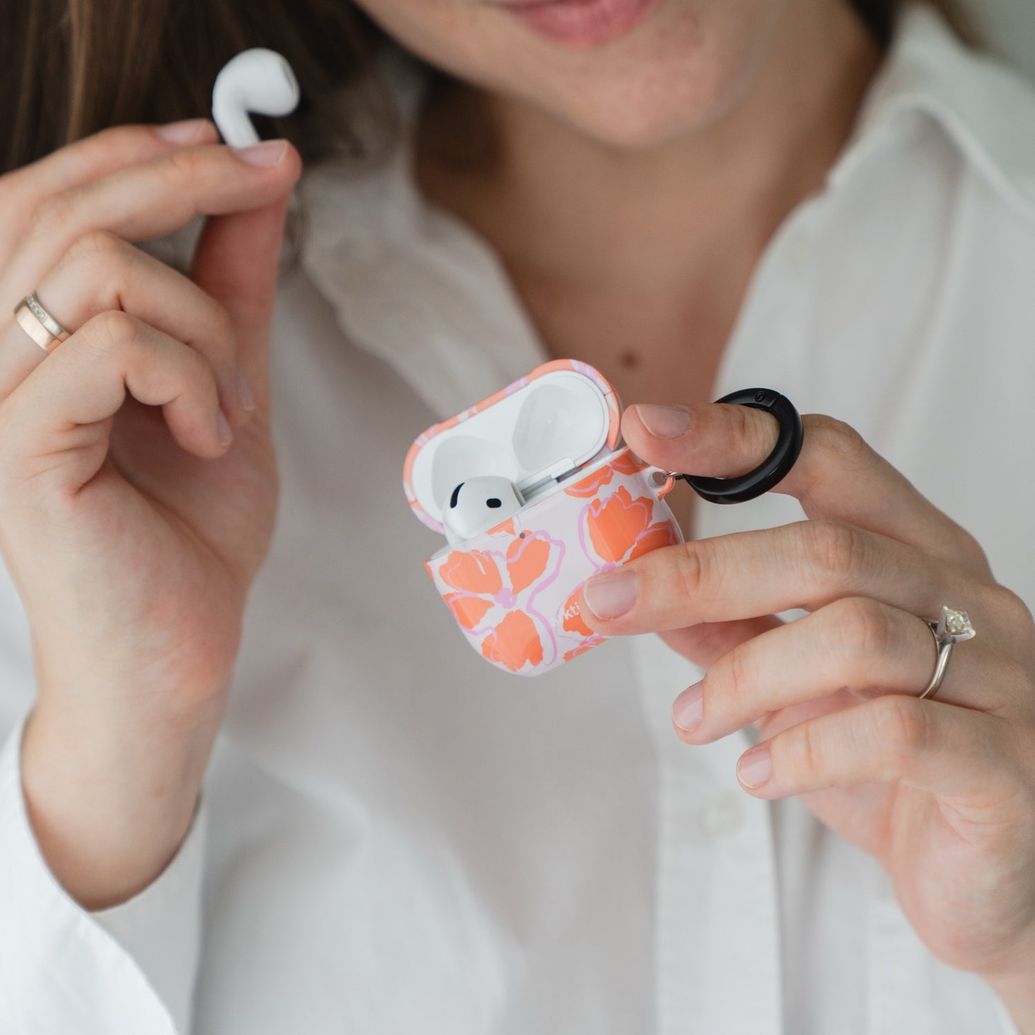Eine Person, die eine Arktis AirPods 5 Hülle – Orange Mallow mit einem schwarzen Befestigungsring in der Hand hält.