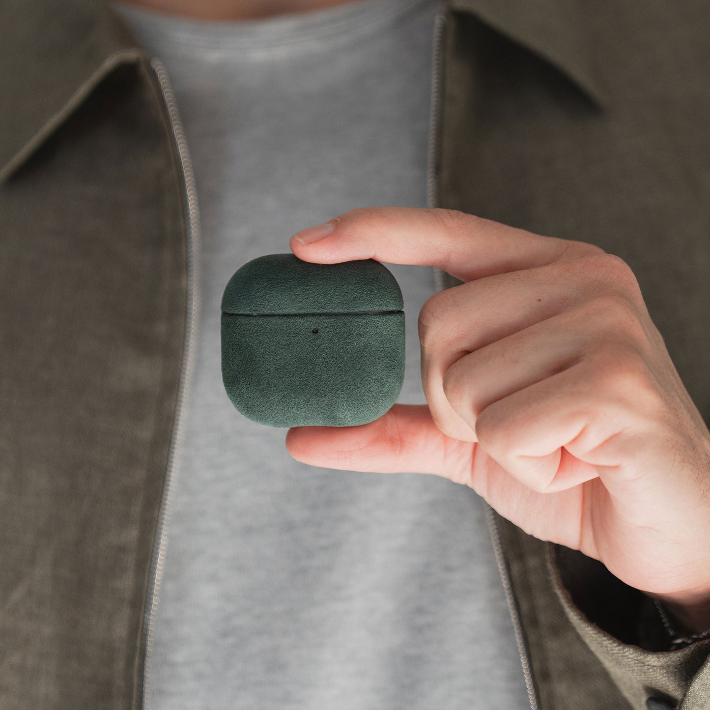 Jemand hält eine grüne Arktis AirPods Pro 3-Hülle aus Alcantara zwischen Daumen und Zeigefinger.