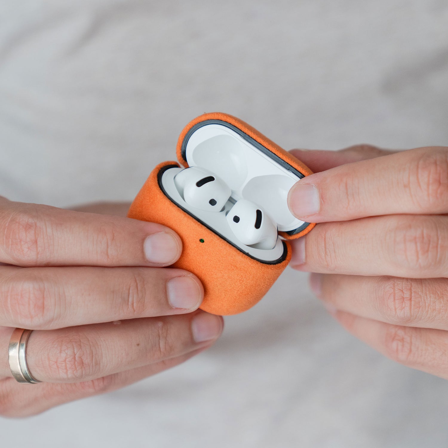 Hände, die eine Arktis AirPods Pro 3-Hülle aus Alcantara in Orange halten; der Deckel ist geöffnet, sodass die darin befindlichen kabellosen Ohrhörer zu sehen sind.