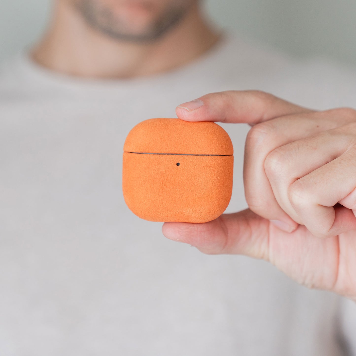 Jemand hält eine orangefarbene Arktis AirPods Pro 3-Hülle aus Alcantara zwischen Daumen und Zeigefinger.