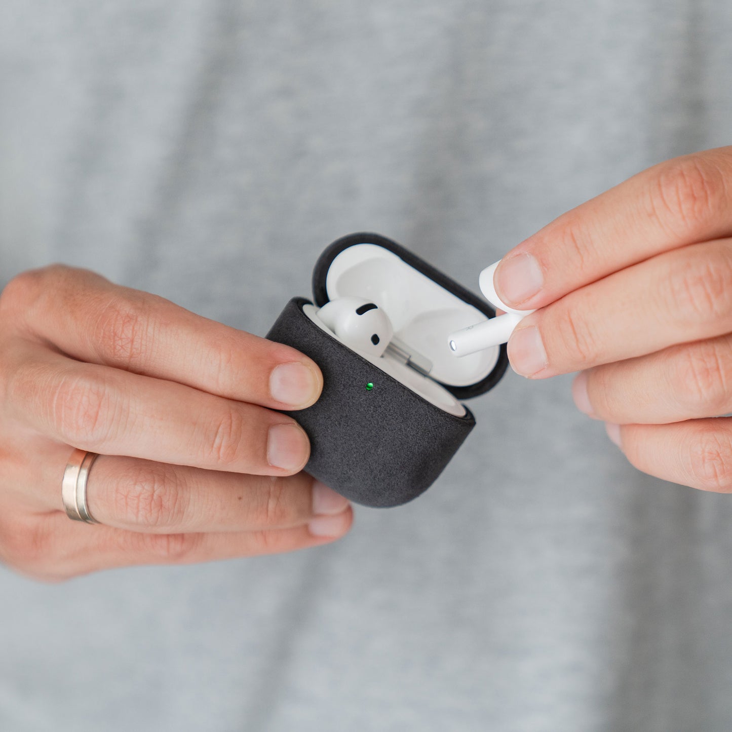 Eine Hand mit einem silbernen Ring nimmt einen Ohrhörer aus der schwarzen Arktis AirPods Pro 3-Hülle aus Alcantara heraus.