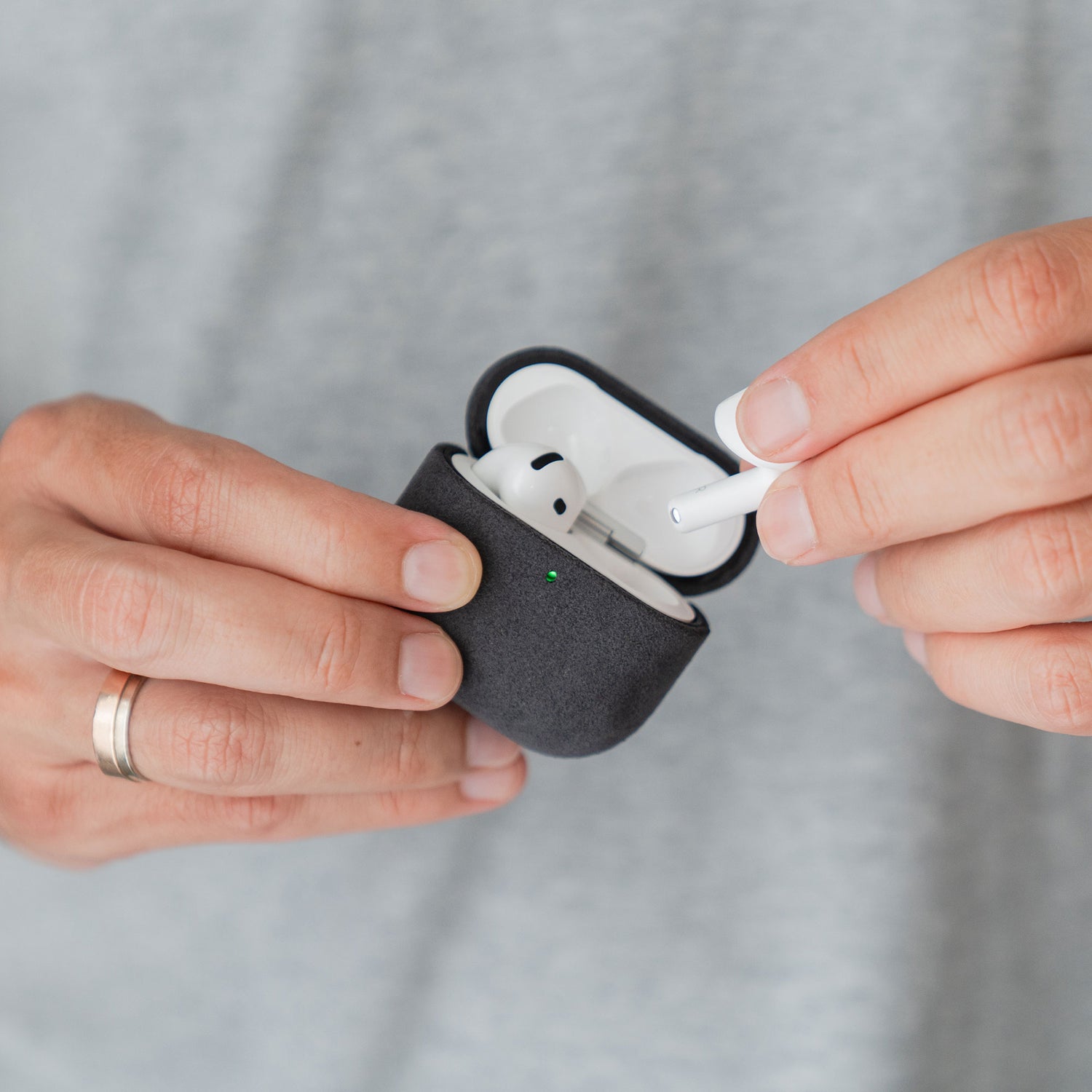 Eine Hand mit einem silbernen Ring nimmt einen Ohrhörer aus der schwarzen Arktis AirPods Pro 3-Hülle aus Alcantara heraus.