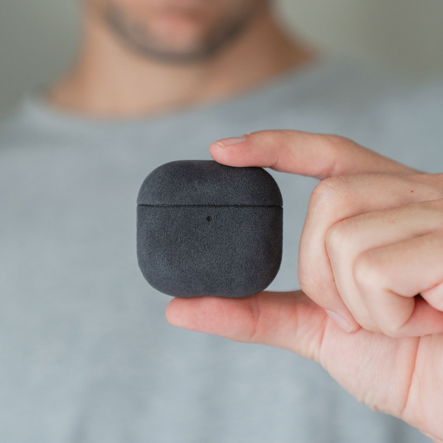 Eine Hand hält die Arktis AirPods Pro 3-Hülle aus Alcantara vor einem unscharfen Hintergrund.