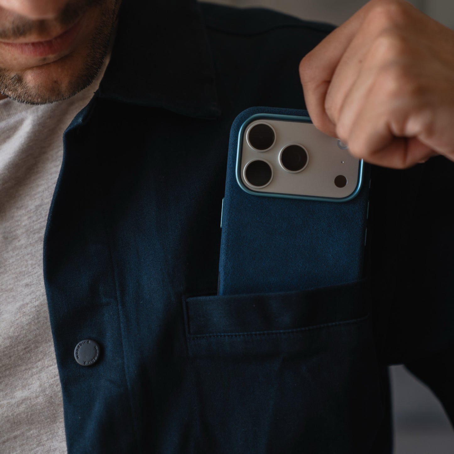 Person steckt ein iPhone 17 Pro mit arktis Hülle aus Alcantara in blauer Farbe in die Brusttasche eines dunklen Jackets.