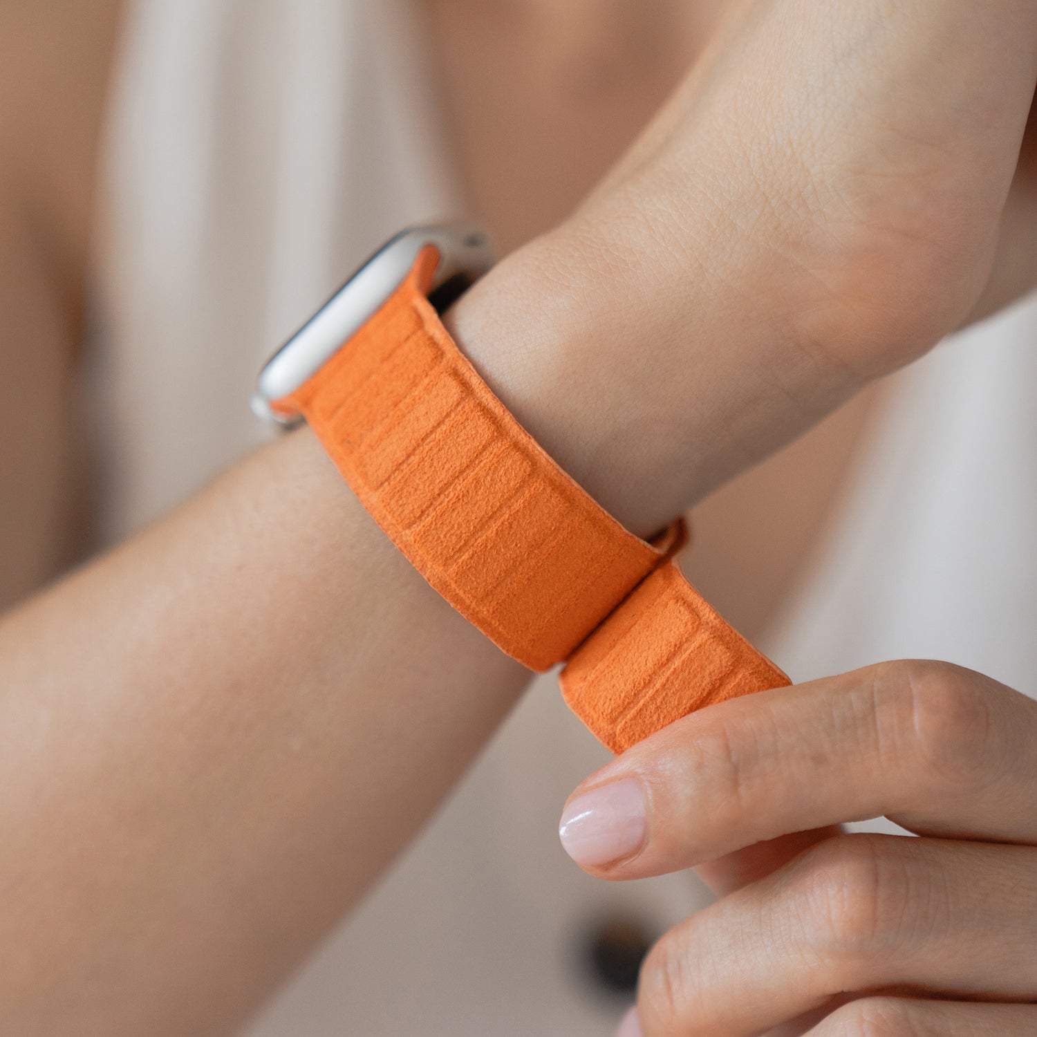 Nahaufnahme einer Person, die ein orangefarbenes Arktisband Apple Watch magnetisches Armband aus Alcantara am Handgelenk befestigt - echter italienischer Stil, kompatibel mit Apple Watch.