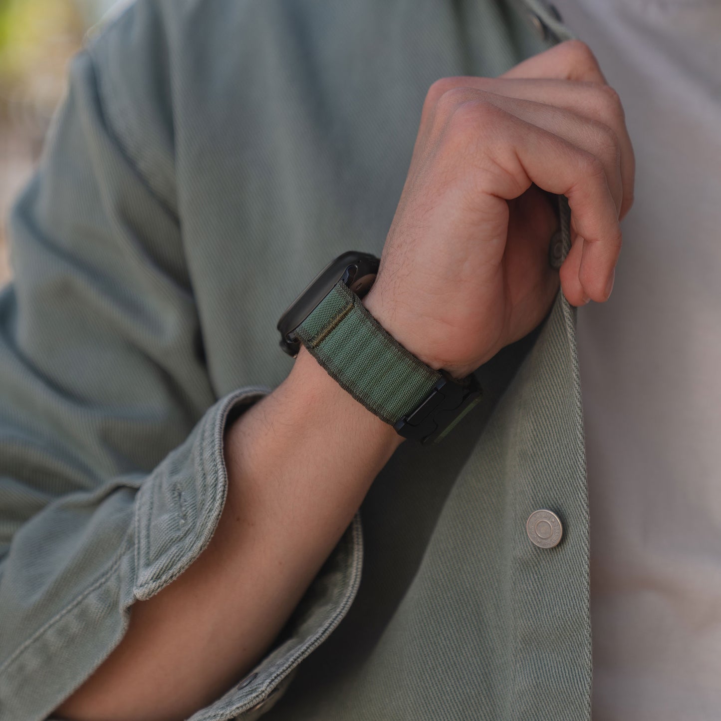 Eine Person trägt eine grüne Jacke und das arktisband Apple Watch Armband "CoreX" von arktisband mit einem grünen Stoff im Wave-Look am Handgelenk.