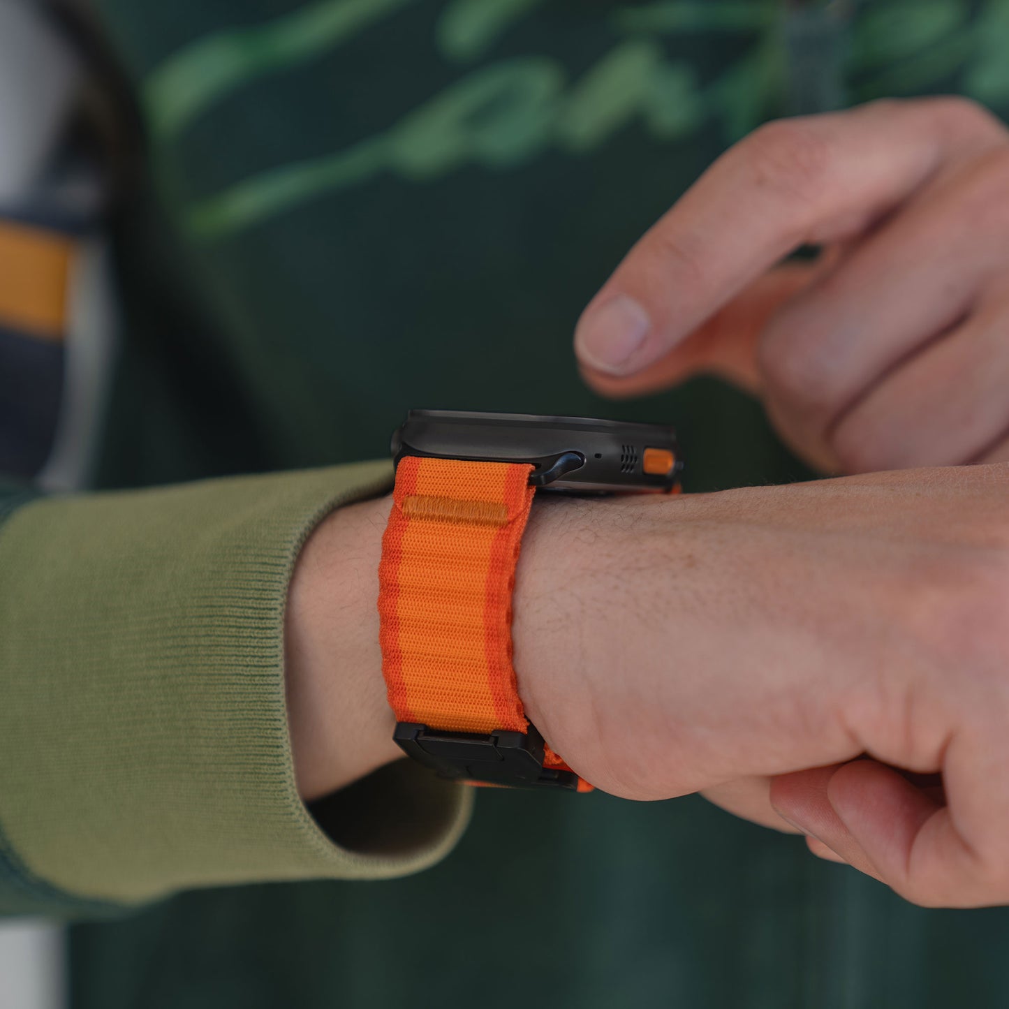 Jemand berührt seine Smartwatch, während er das arktisband Apple Watch Armband "CoreX" von arktisband mit orangefarbenem Stoffband und Parachute-Verschluss trägt.