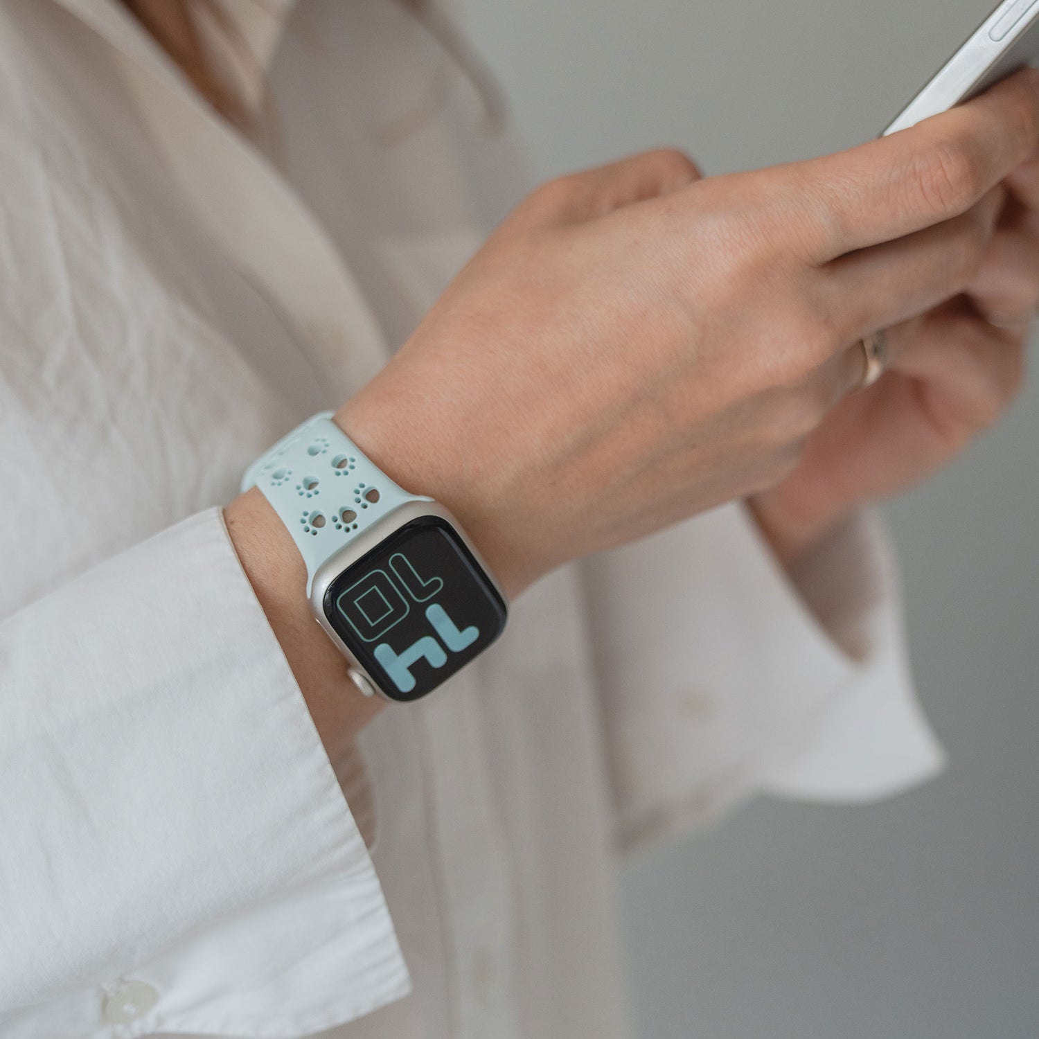 Person im weißen Hemd, die ein Smartphone benutzt und ein Arktisband Apple Watch Silikonarmband "Paw" trägt.
