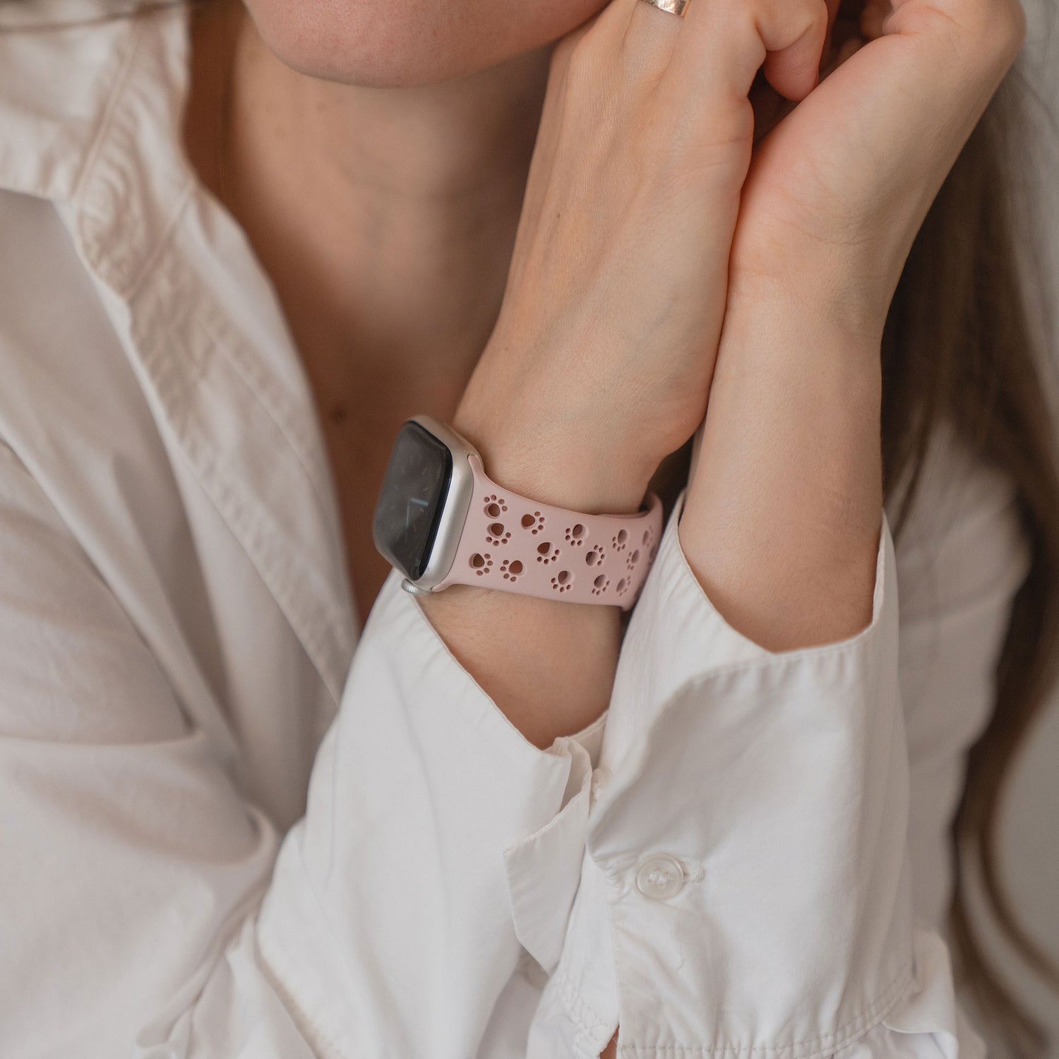 Eine Frau trägt ein weißes Hemd und ein Arktisband Apple Watch Silikonarmband "Paw" in Rosa mit Perforationen, wobei sie ihre Hände zusammenlegt.