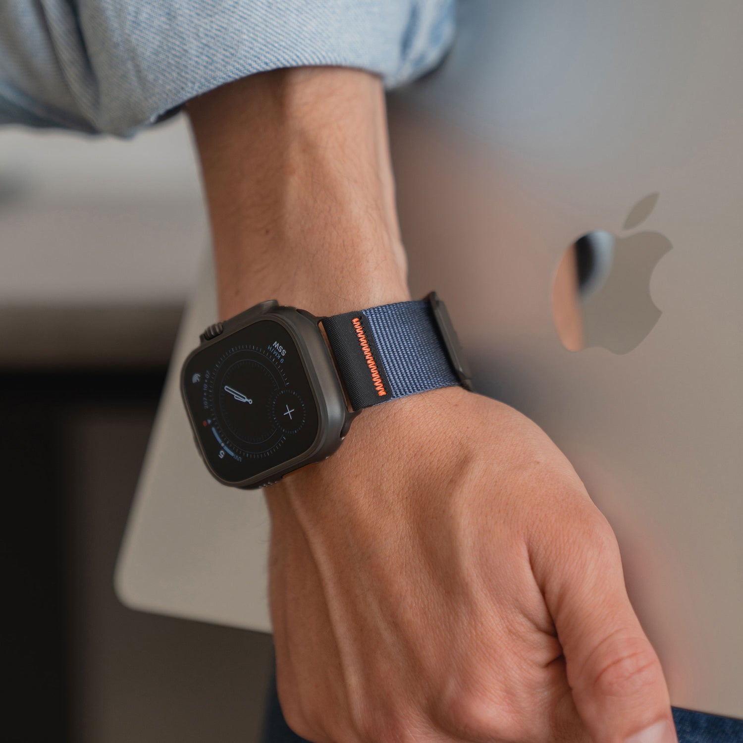 Eine Person, die ein blaues Arktisband Apple Watch Armband "Terra" trägt, hält einen silbernen Apple Laptop unter ihrem Arm.
