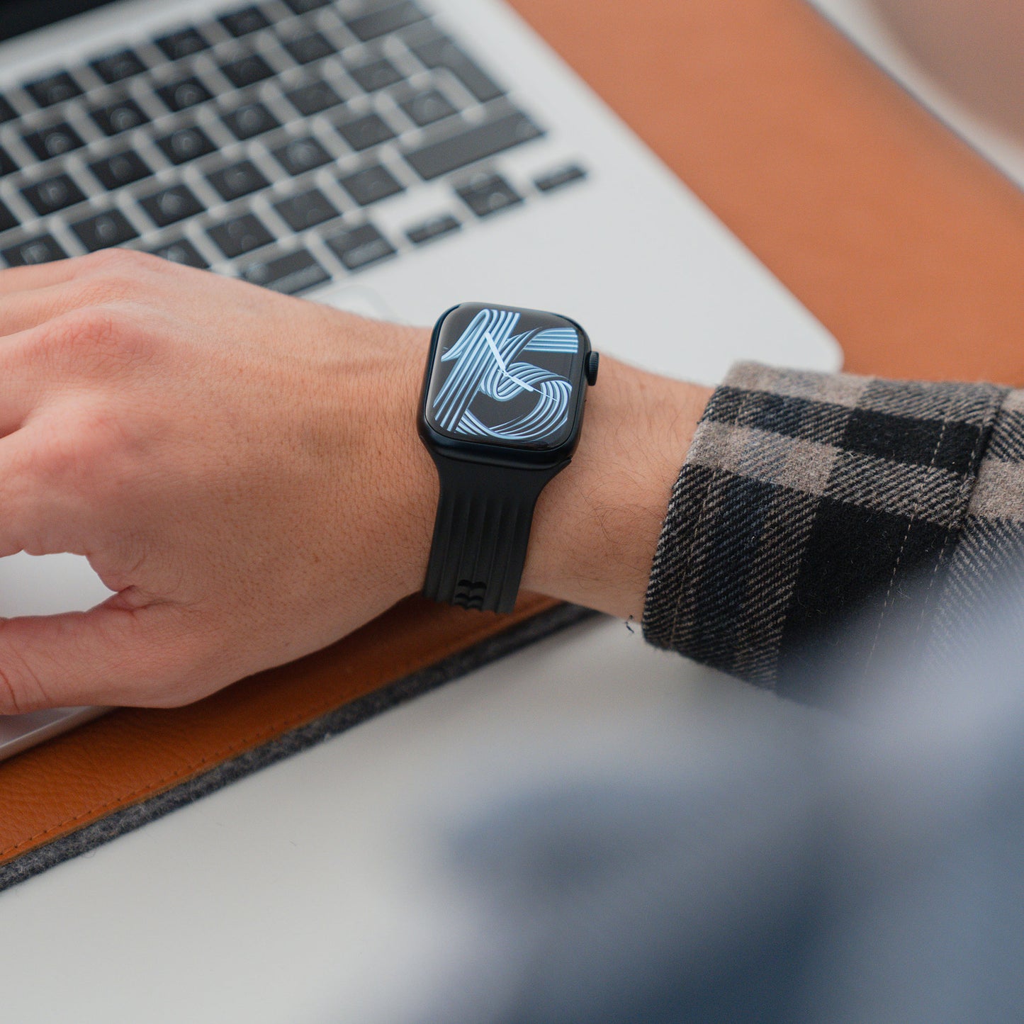 Jemand, der das arktisband Apple Watch Armband "Skandi" von arktisband trägt, benutzt einen Laptop, wobei beide Geräte auf einer braunen Schreibtischunterlage im echten Skandi Design platziert sind.