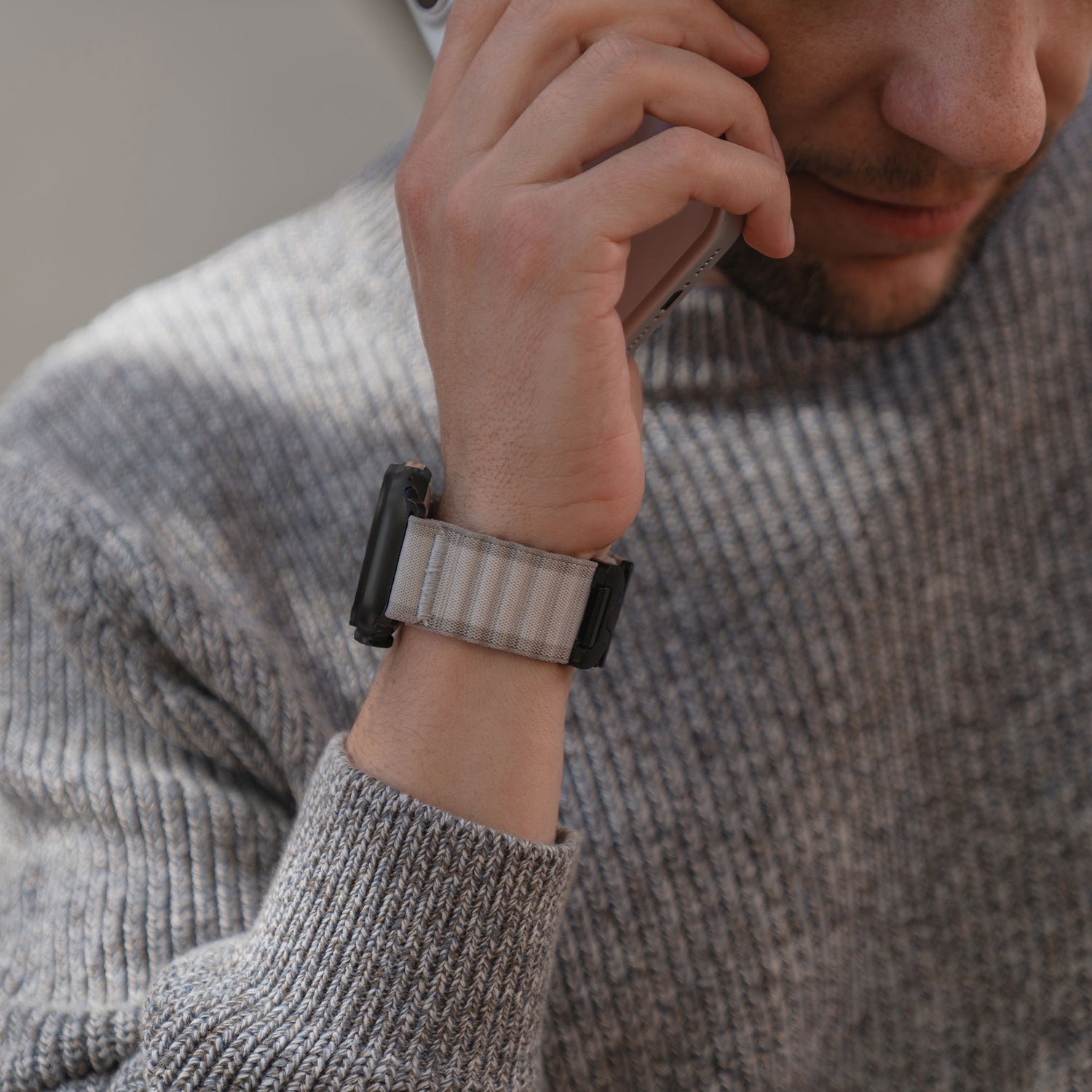 Ein Mann, der einen grauen Pullover und ein arktisband Apple Watch Armband "CoreX" von arktisband trägt, hält ein Telefon an sein Ohr und lächelt leicht.