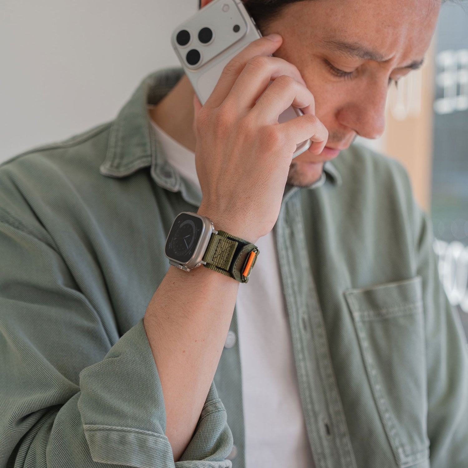 Ein Mann mit grüner Jacke, der mit seinem Smartphone telefoniert, zeigt seinen Outdoor-Stil mit dem arktisband Apple Watch Outdoor Armband "Forge" von arktisband.