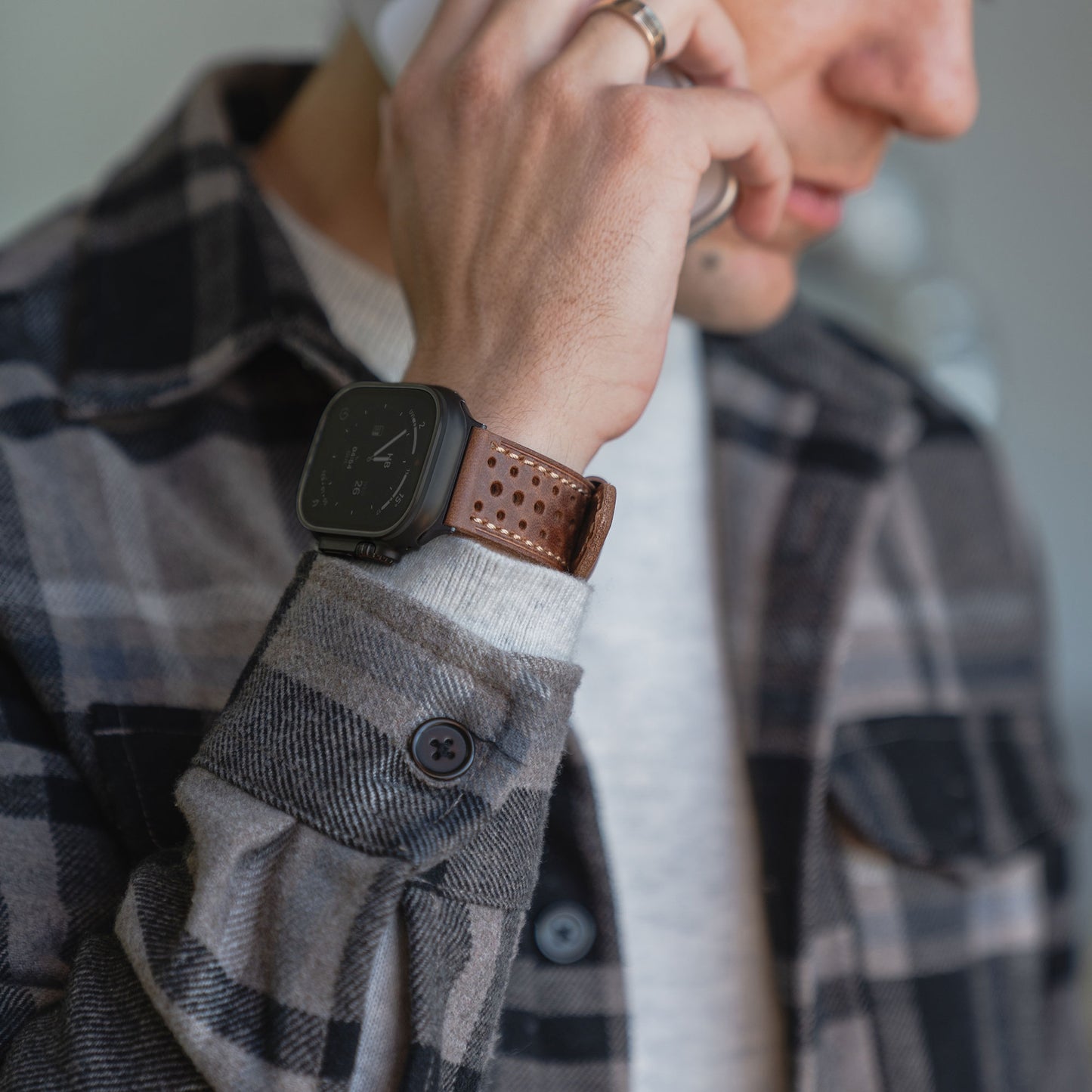 Mann mit kariertem Hemd und arktisband Apple Watch Lederarmband "Toronto" von arktisband, hält sich ein Telefon ans Ohr und spricht.