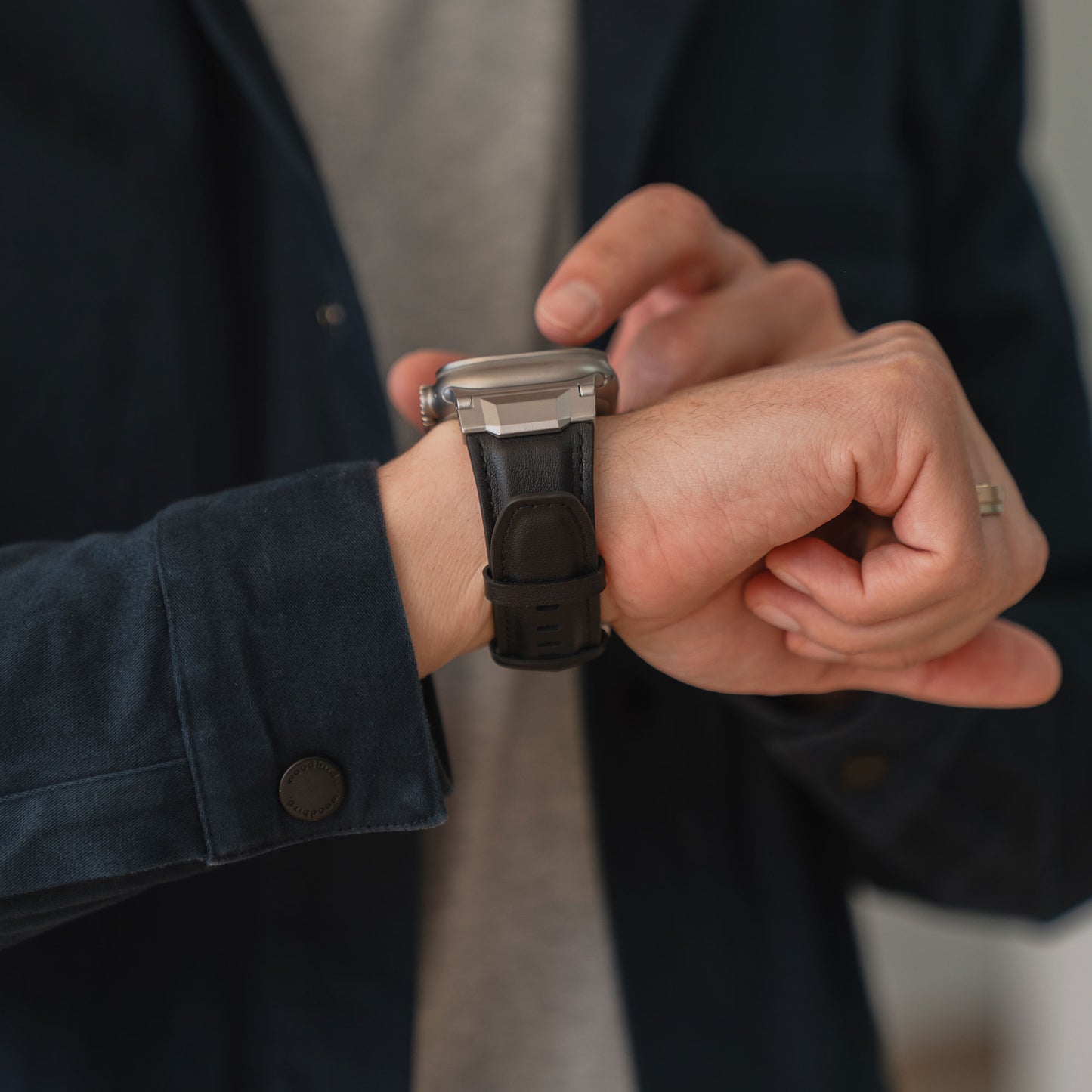 Person in dunkler Jacke tippt mit der anderen Hand auf ein Arktisband Apple Watch Ultra Lederarmband "Delta" an ihrem Handgelenk.