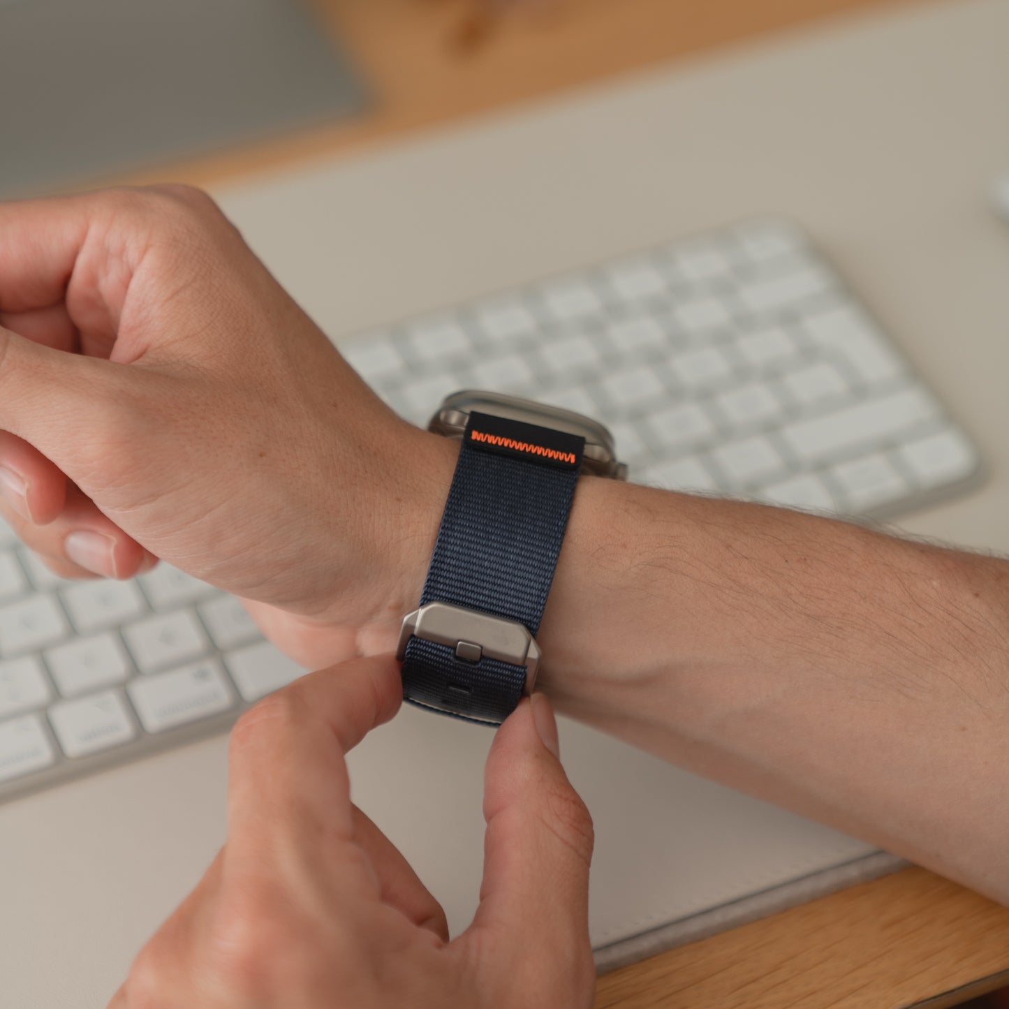 Nahaufnahme einer Person, die ein arktisband Apple Watch Armband "Terra" mit extra breitem 24-mm-Nylonband an ihrem Handgelenk in der Nähe einer Computertastatur befestigt.