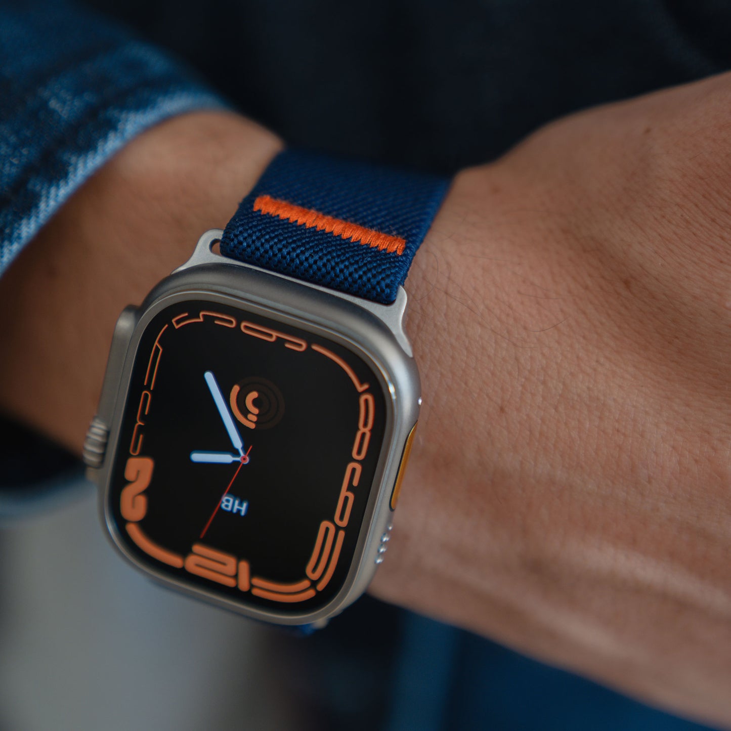Eine Nahaufnahme eines Arktisbandes Apple Watch Nylonarmband "FlexOne" in Blau und Orange am Handgelenk einer Person.