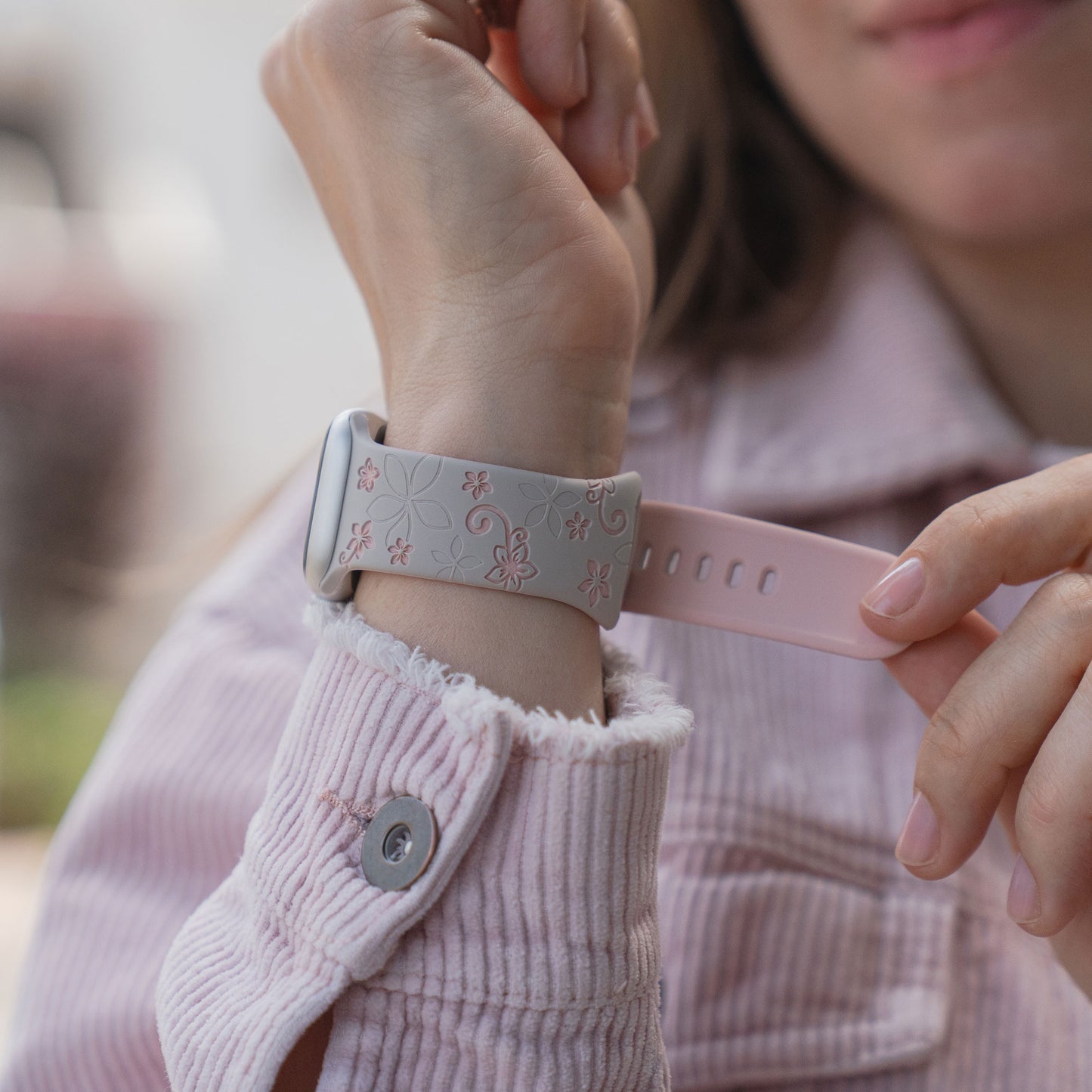 Eine Frau in einer rosa Jacke befestigt ein arktisband Apple Watch Silikonarmband "Bloom" von arktisband an ihrem Handgelenk.