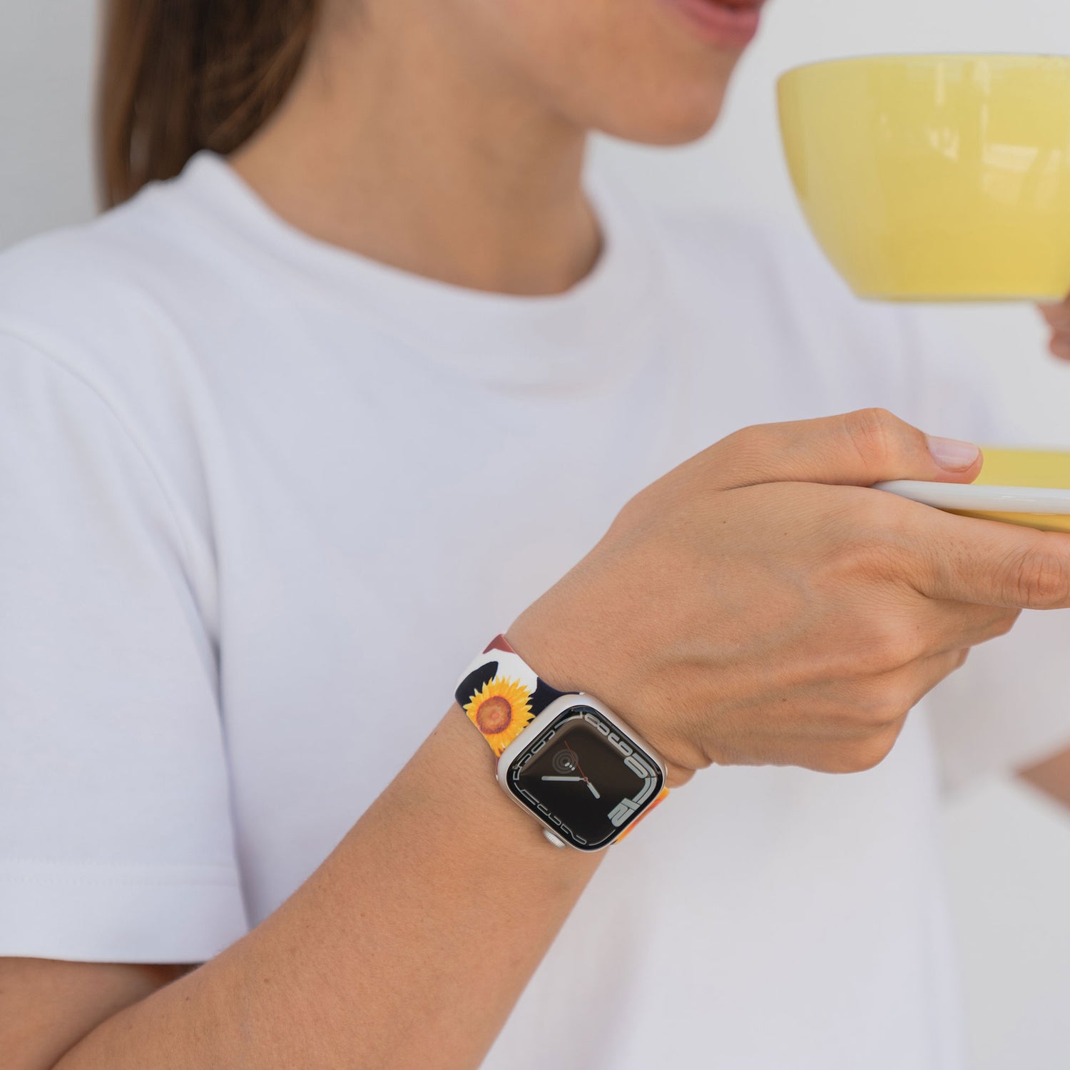 Eine Person im weißen Hemd hält eine gelbe Tasse und trägt die arktisband EDITION für Apple Watch von arktisband mit Sonnenblumenmuster für einen stilvollen Touch.