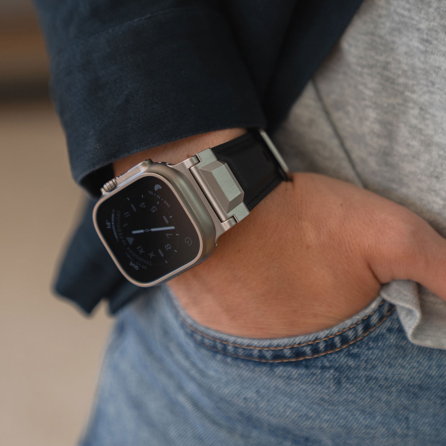Eine Person mit einer arktisband Apple Watch Ultra Lederarmband "Delta" von arktisband, schwarzes Band sichtbar, Hand in der Tasche, trägt Jeans und ein graues Hemd.