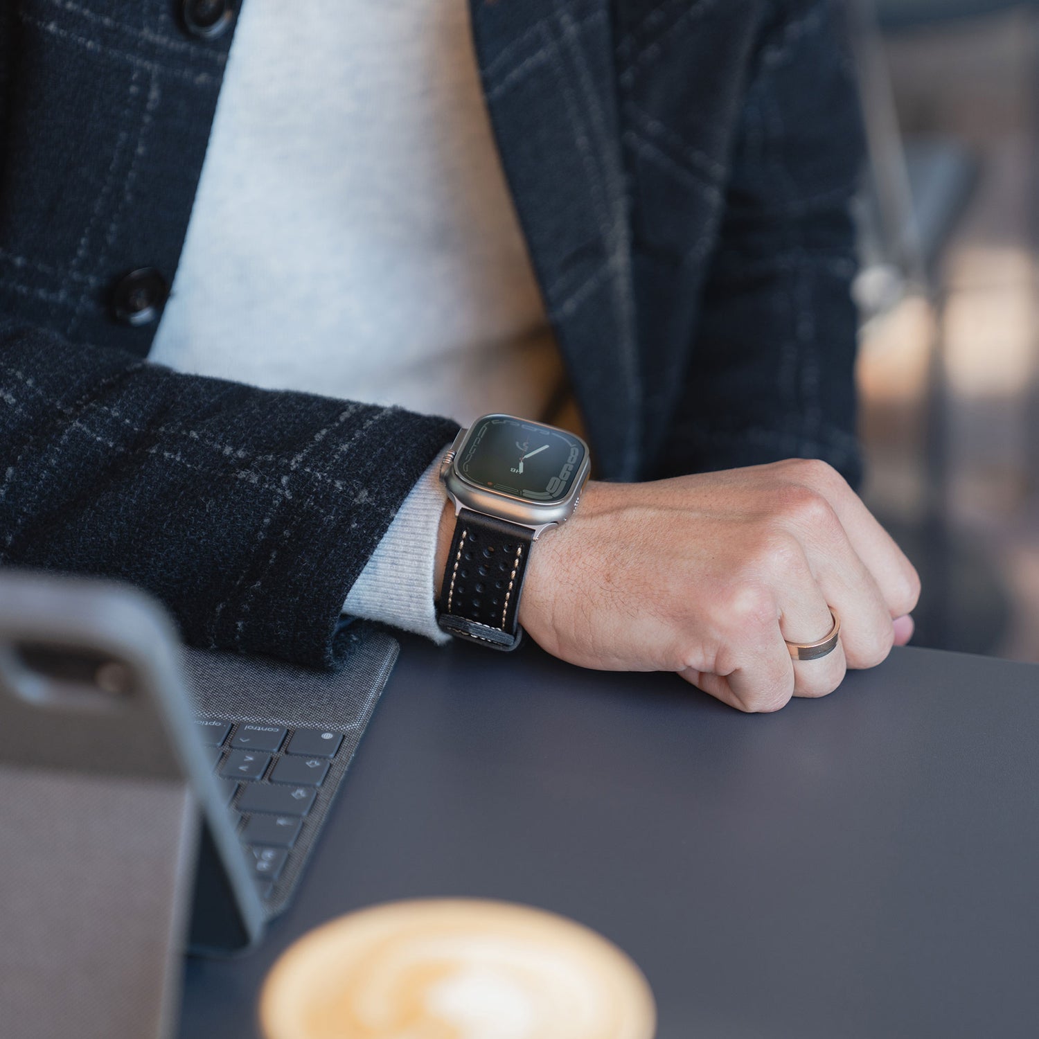 Eine Person, die das arktisband Apple Watch Lederarmband "Toronto" trägt, sitzt in einem Blazer mit einem Tablet und einer Kaffeetasse an einem Schreibtisch und zeigt den raffinierten Stil und das Vintage-inspirierte Design von arktisband.