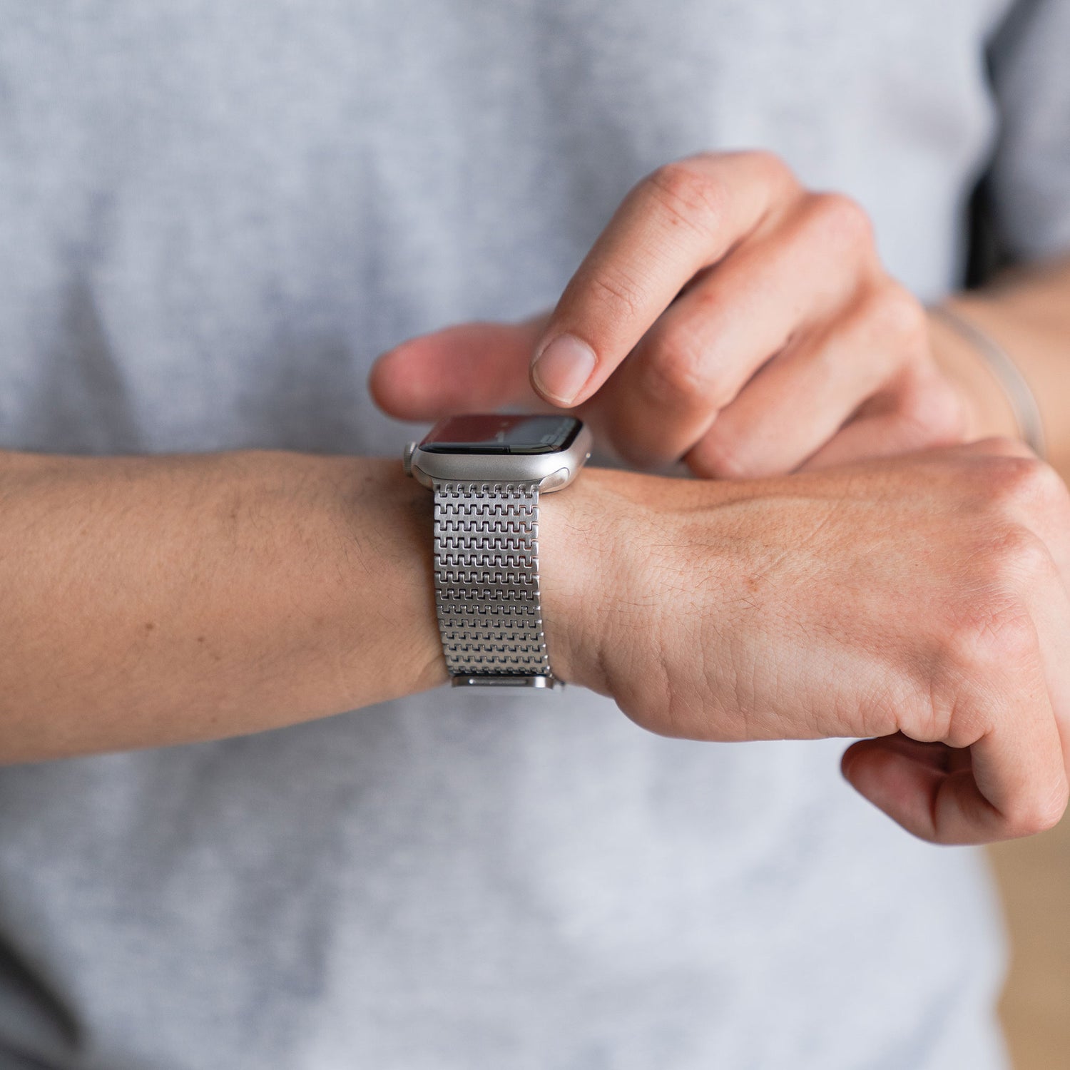 Jemand trägt ein arktisband Apple Watch Edelstahlarmband „Aurora“ von arktisband in Silber und tippt mit der anderen Hand auf das Display.