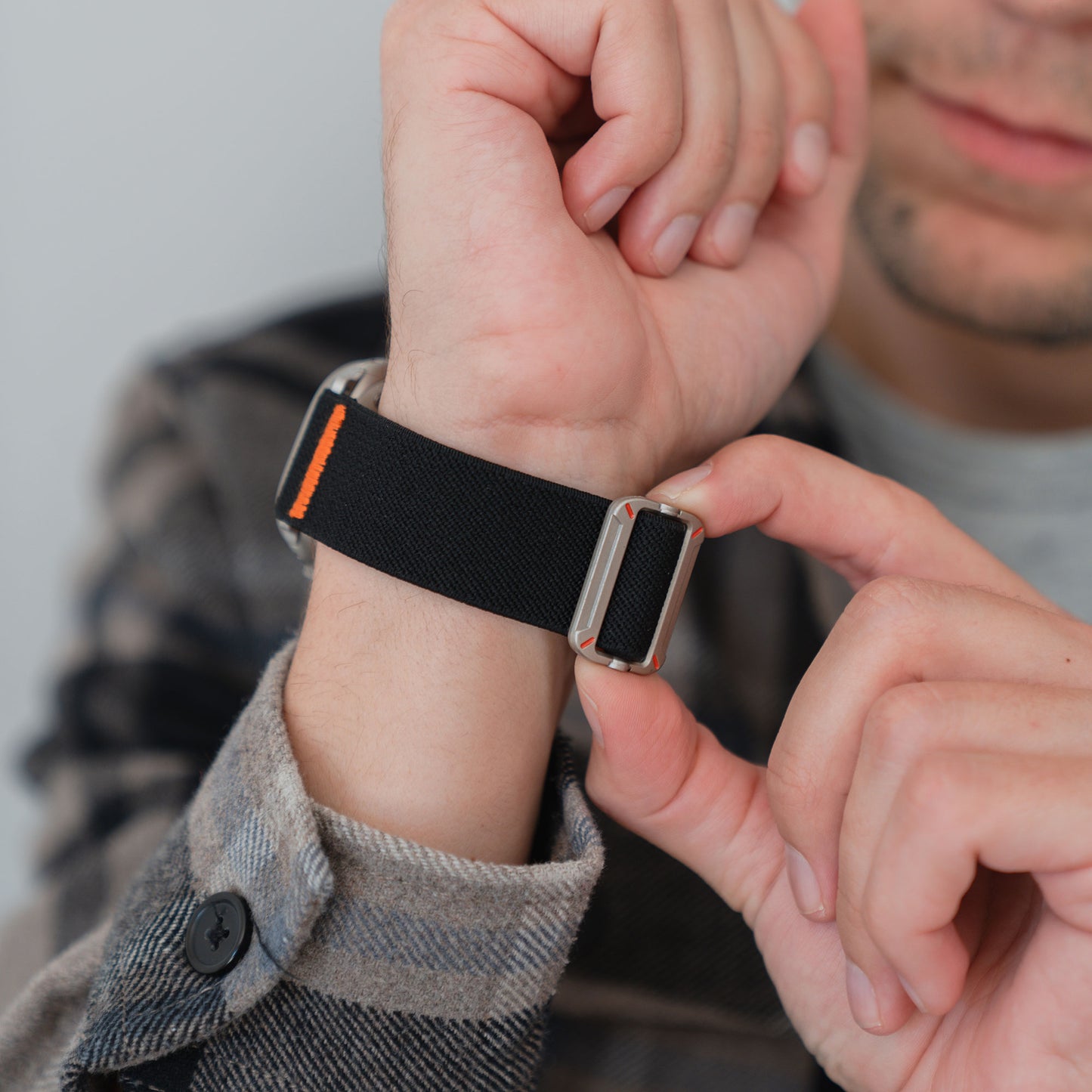 Eine Person legt sich ein arktisband Apple Watch Nylonarmband "FlexOne" in schwarz mit Metallschließe um das Handgelenk, ideal für die Verwendung als Apple Watch Band.