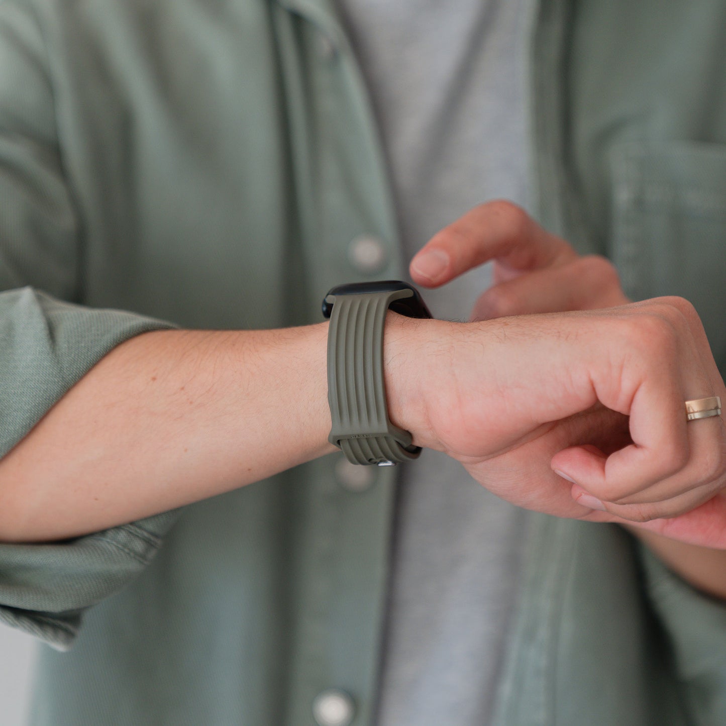 Eine Person in einem von Skandi inspirierten grünen Hemd und grauen T-Shirt berührt den Bildschirm ihres arktisband Apple Watch Armbands "Skandi" von arktisband mit einem Band aus Fluorelastomer.