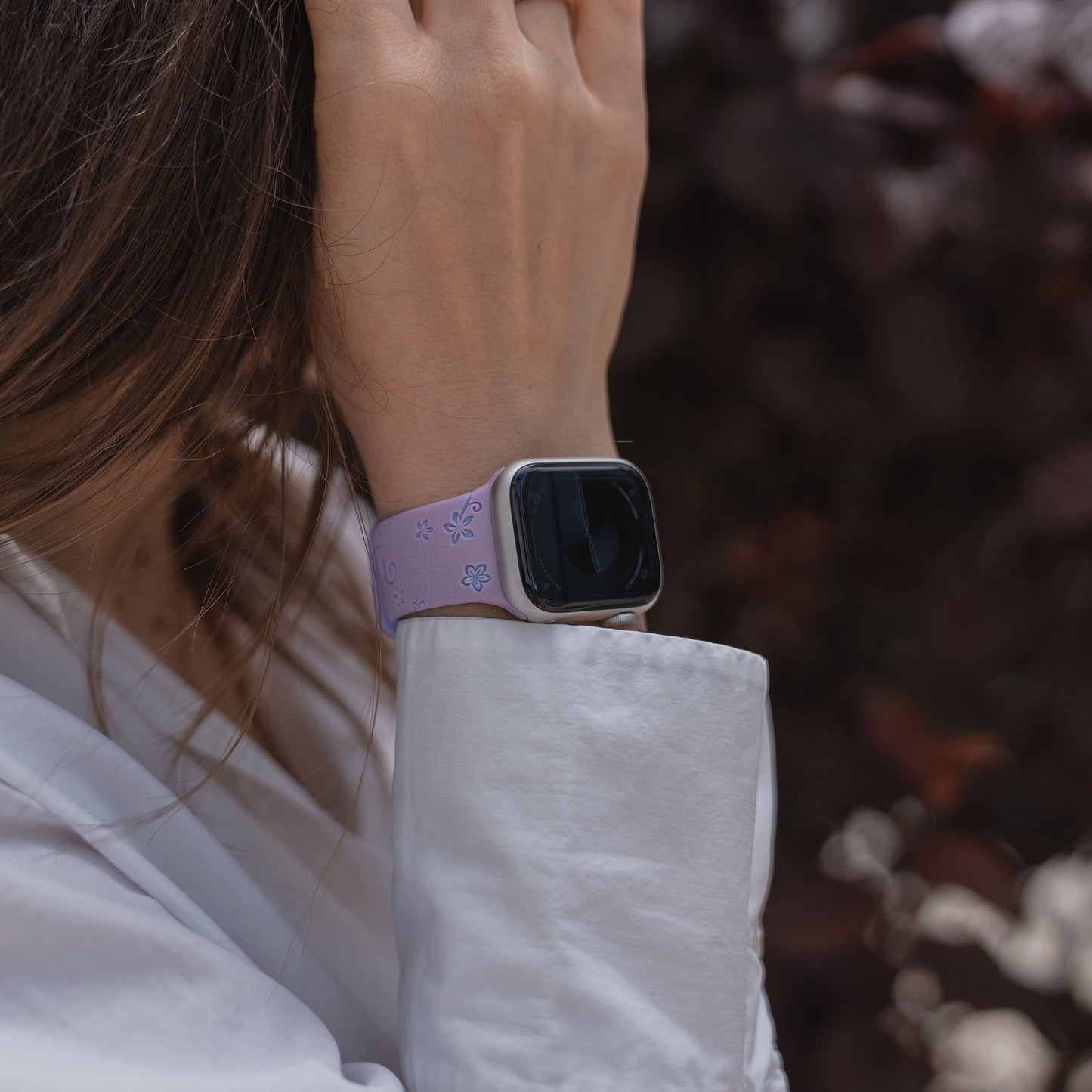 Person mit weißem Shirt trägt ein arktisband Apple Watch Silikonarmband "Bloom" von arktisband und berührt ihr Haar.