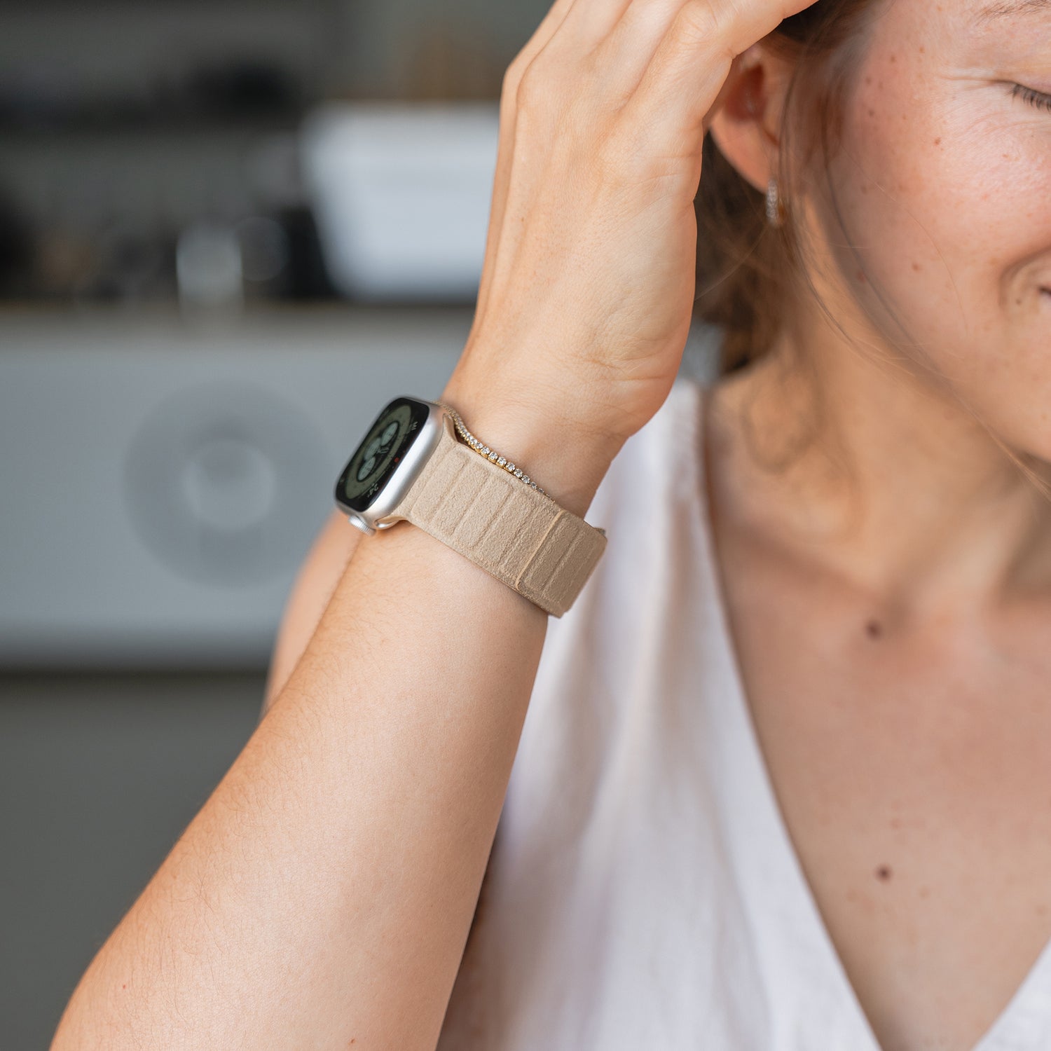Eine Frau trägt ein Apple Watch magnetisches Armband aus Alcantara mit einem beigen Armband, hält ihre Hand an ihr Gesicht und lächelt teilweise.