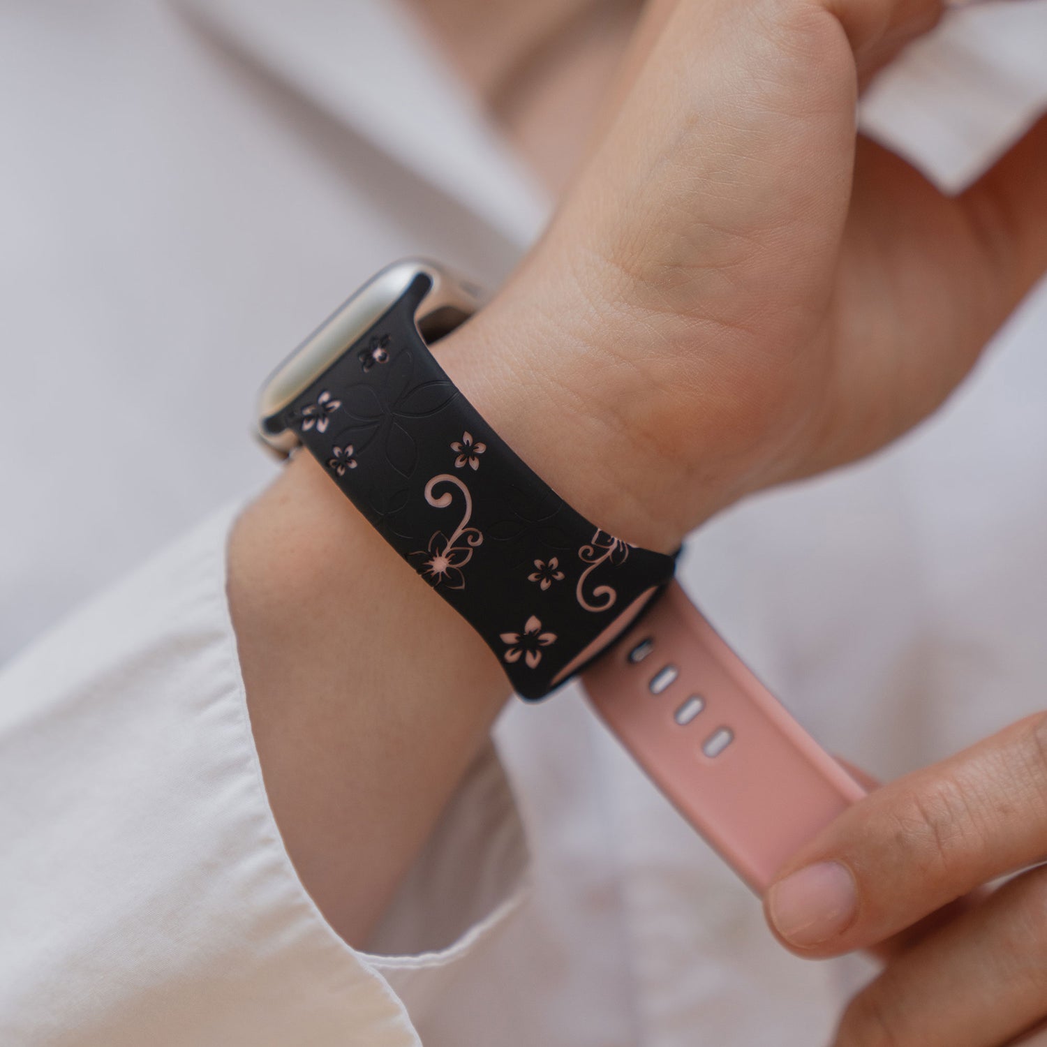 Jemand trägt das arktisband Apple Watch Silikonarmband "Bloom", ein schwarzes und rosafarbenes Band im Blumendesign von arktisband, an seinem Handgelenk.