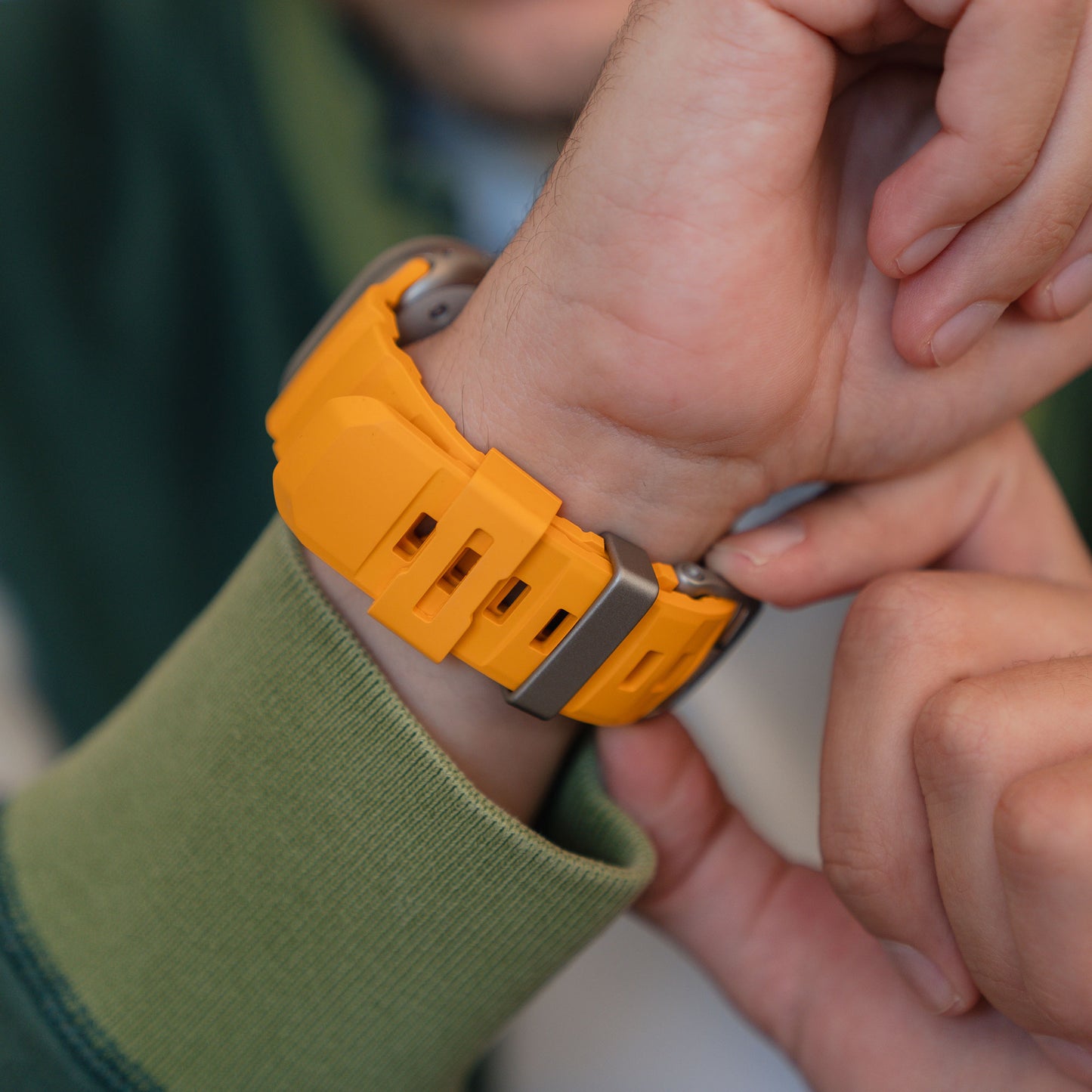 Nahaufnahme einer Person, die ein arktisband Apple Watch Armband "Flux" in gelbem FKM mit Edelstahl Schließe an ihrem linken Handgelenk anpasst.