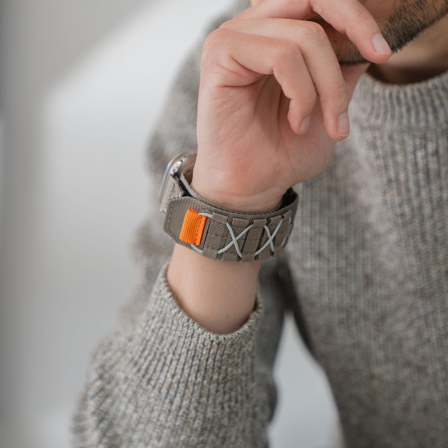 Nahaufnahme einer Person, die einen grauen Strickpullover und das arktisband Apple Watch Outdoor Armband "Forge" von arktisband mit orangen und weißen Details trägt.