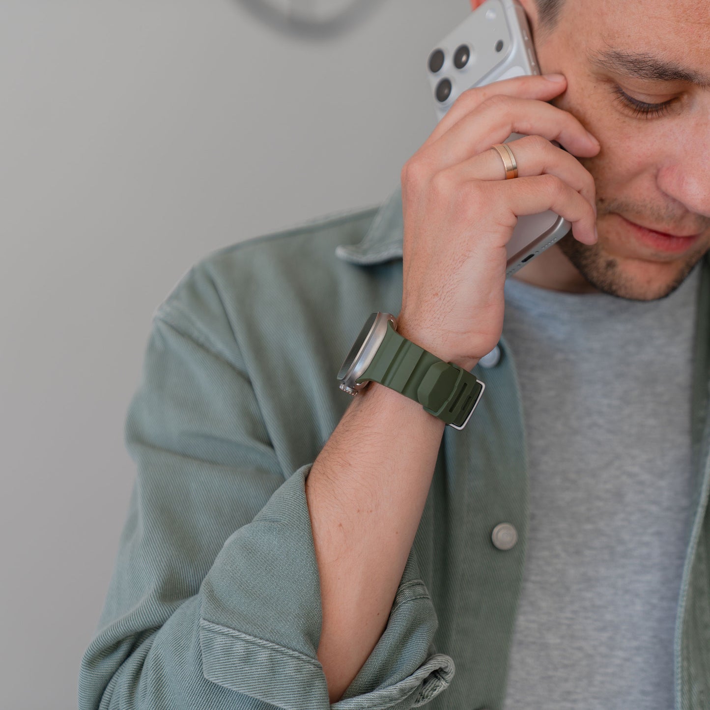 Ein Mann, der eine grüne Jacke und ein Arktisband Apple Watch Armband "Flux" an seiner Smartwatch trägt, spricht mit einem Smartphone, wobei nur ein Teil seines Gesichts zu sehen ist.