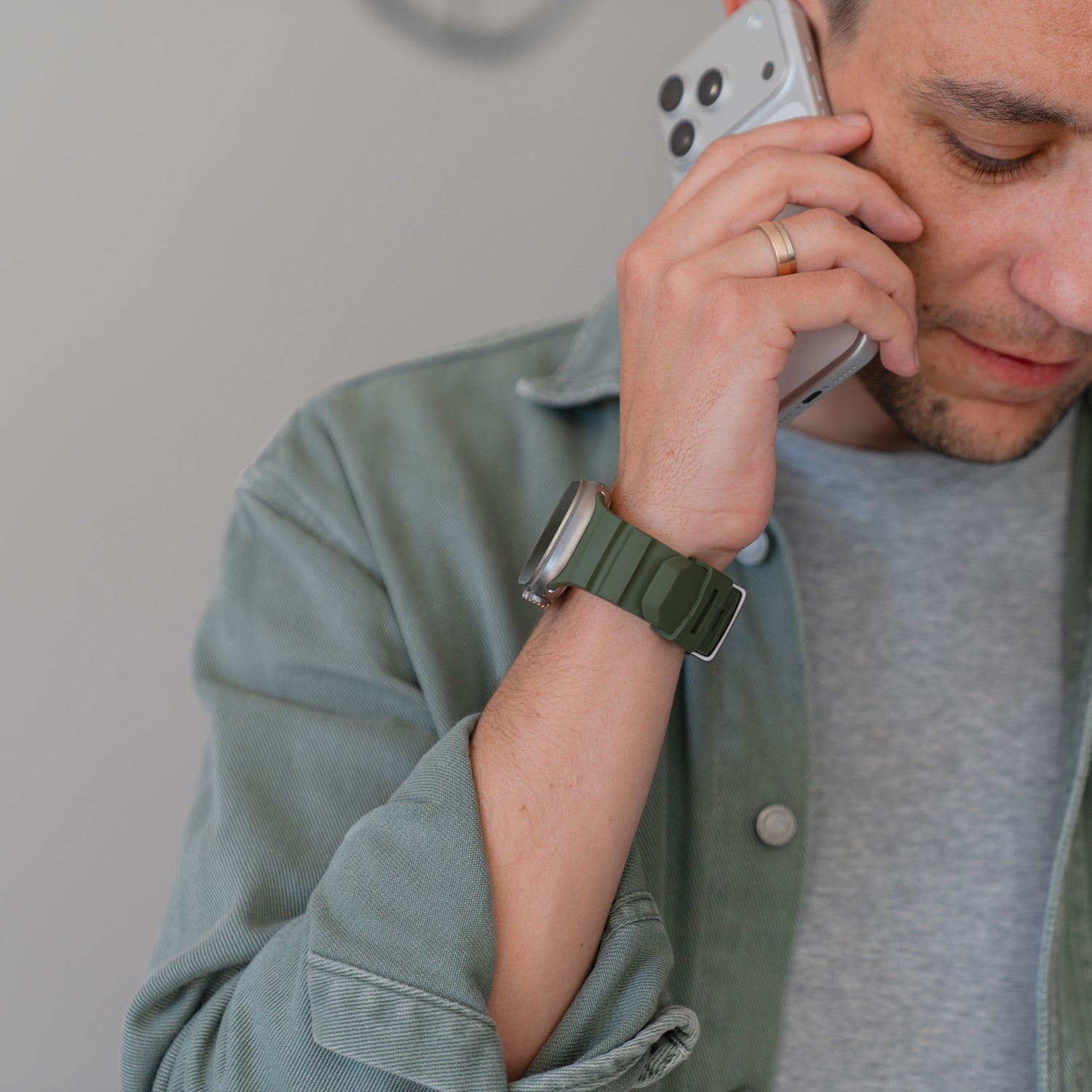 Ein Mann, der eine grüne Jacke und ein Arktisband Apple Watch Armband "Flux" an seiner Smartwatch trägt, spricht mit einem Smartphone, wobei nur ein Teil seines Gesichts zu sehen ist.